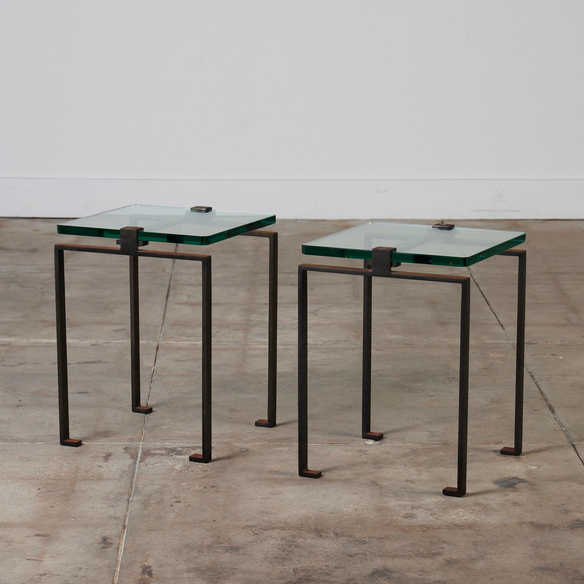 A pair of glass and oxidized steel side tables in the style of Jacques Quinet, c.1980's. The simplistic square shaped tables features a thick green glass. The glass is 