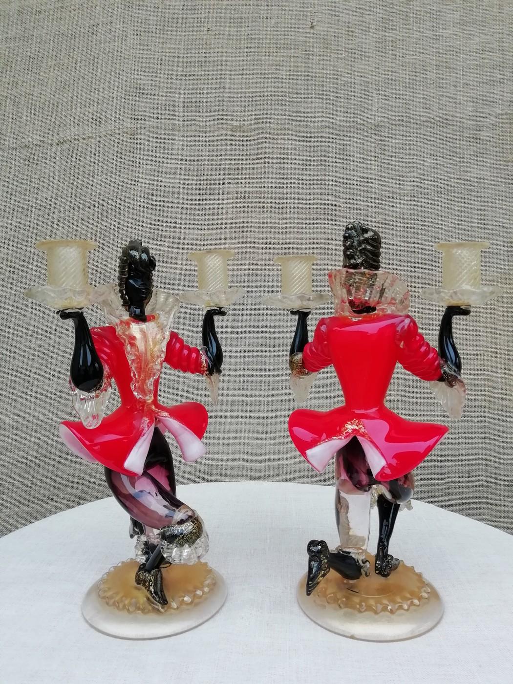 Pair of spun glass candleholders representing two figures wearing red 18th century period outfits. Kneeling on a gilded base, they hold a candle in each of their hands.
Italy Venice, circa 1950.