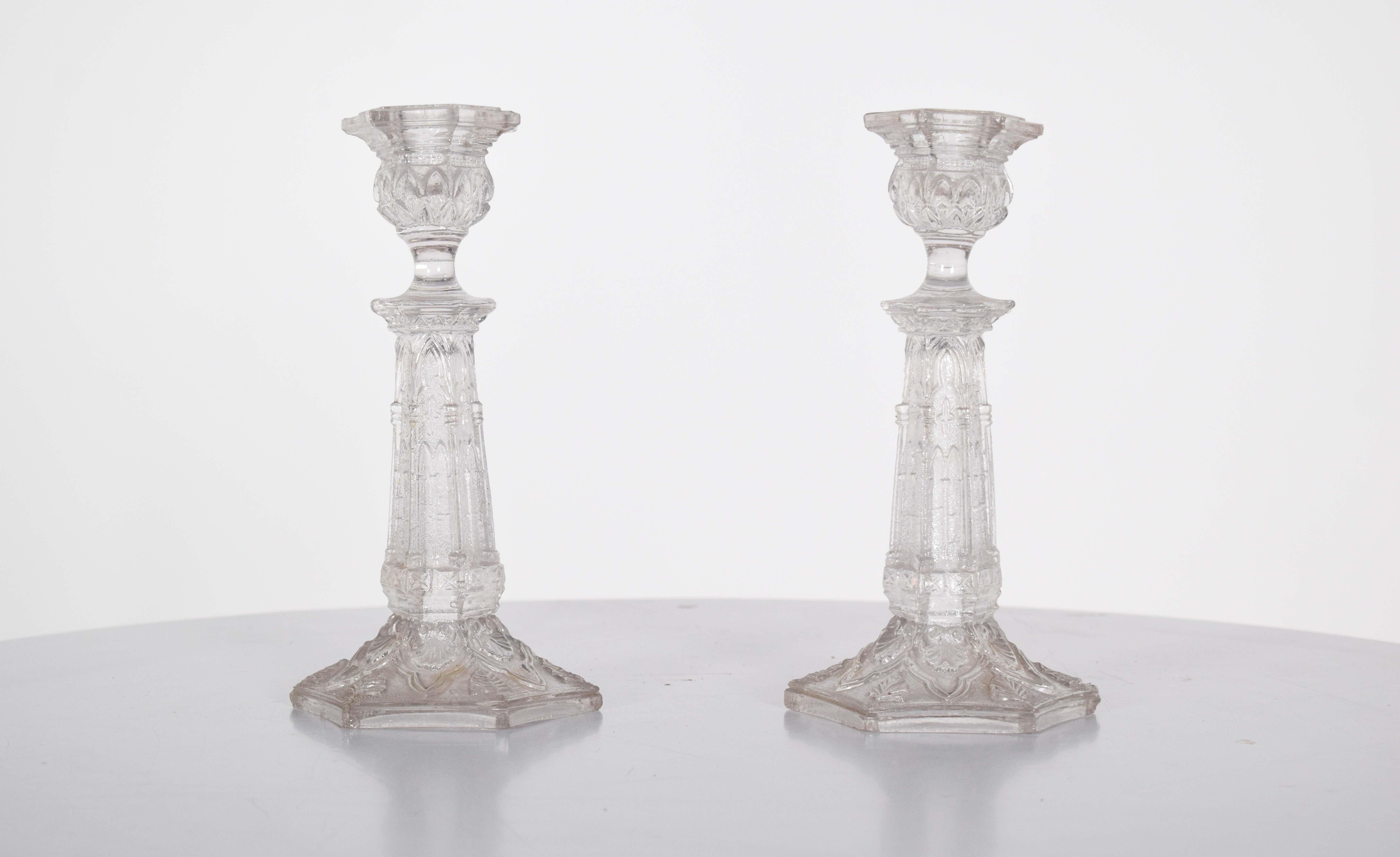 This elegant pair of glass candlesticks features intricate relief work, adding texture and dimension to their refined design. Each candlestick stands tall with a hexagonal base, providing both stability and a unique geometric appeal. The relief work