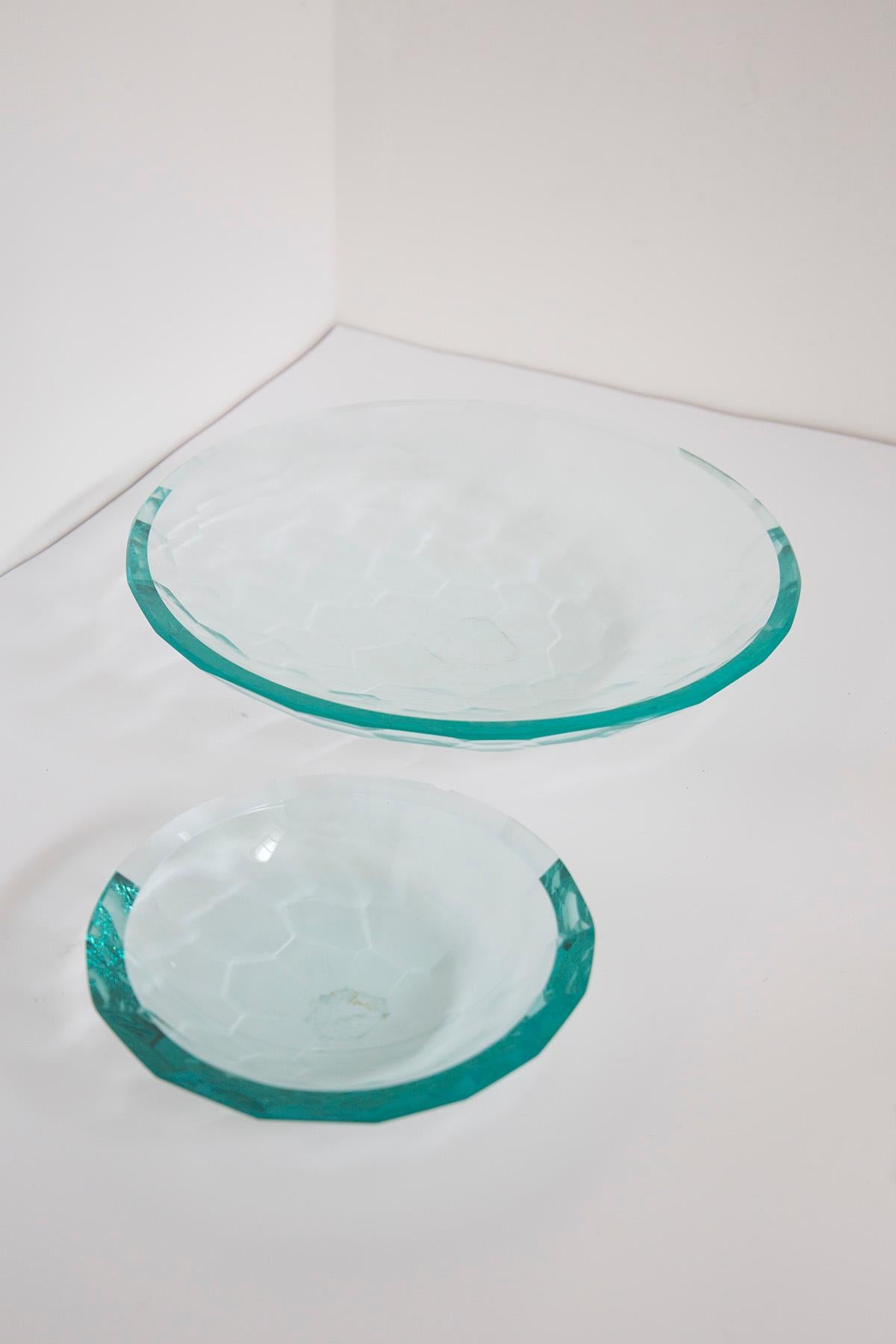 Elegant pair of centerpieces made of thick glass using a hand-tabbed technique. The pair is in the style of the great Fontana Arte manufacture made in the 1980s.
In the pair we find two bowls one larger and one smaller. The thick glass creates color