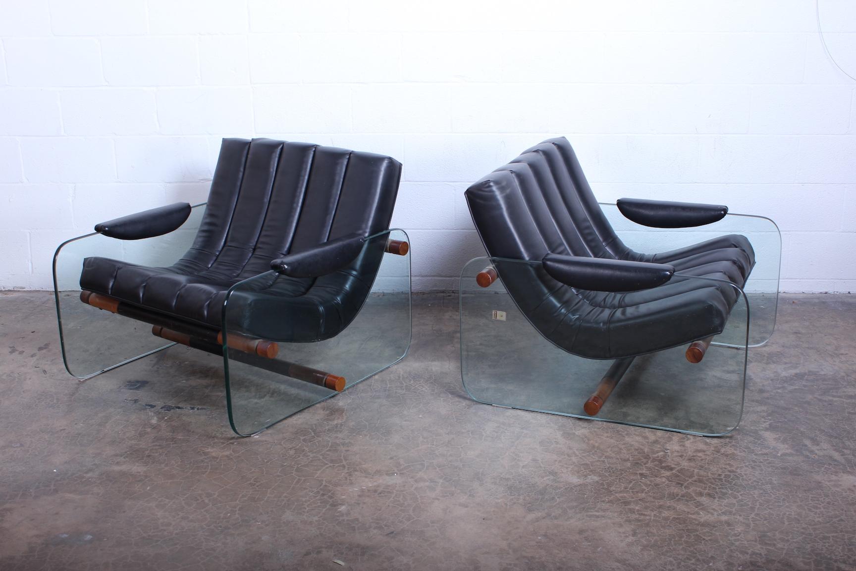 A pair of glass sided lounge chairs by Mirox with original black vinyl upholstery.