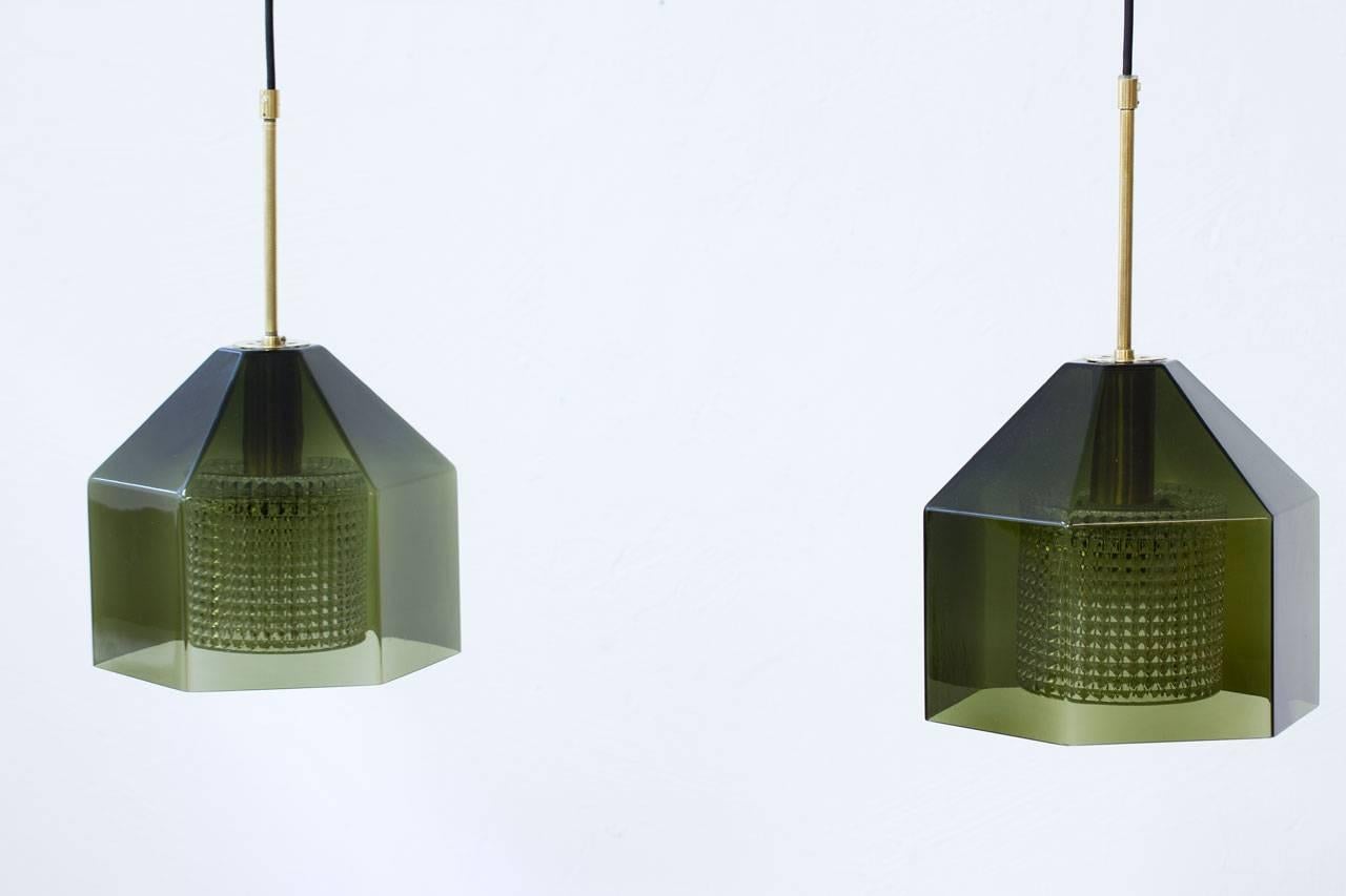 Pair of pendant lamps designed by Carl Fagerlund for Swedish glass company Orrefors during the 1960s. Hexagon shaped outer cup of green tinted glass with internal diffuser in clear pressed glass. Polished brass fittings, new electricity with black