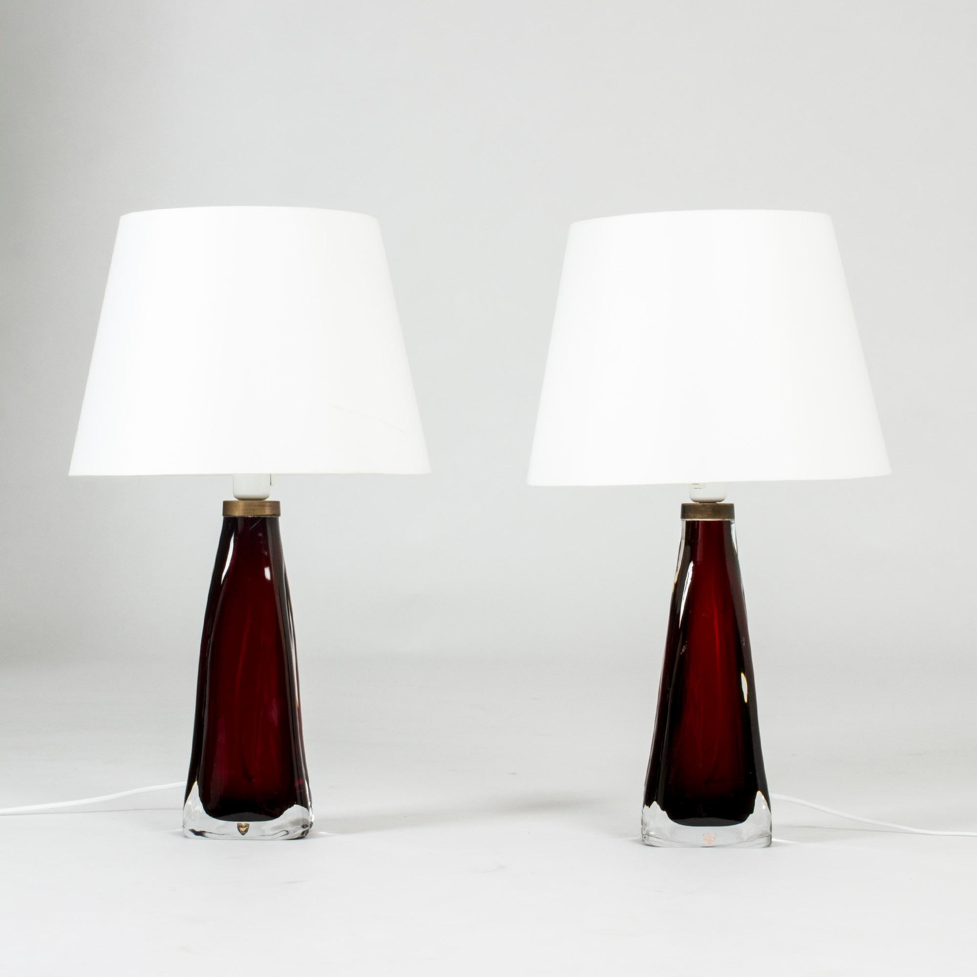 Pair of stunning dark, rich red, semi-translucent glass table lamps by Carl Fagerlund for Orrefors. Heavy glass bases with a somewhat undulating shape and brass detail at the top.