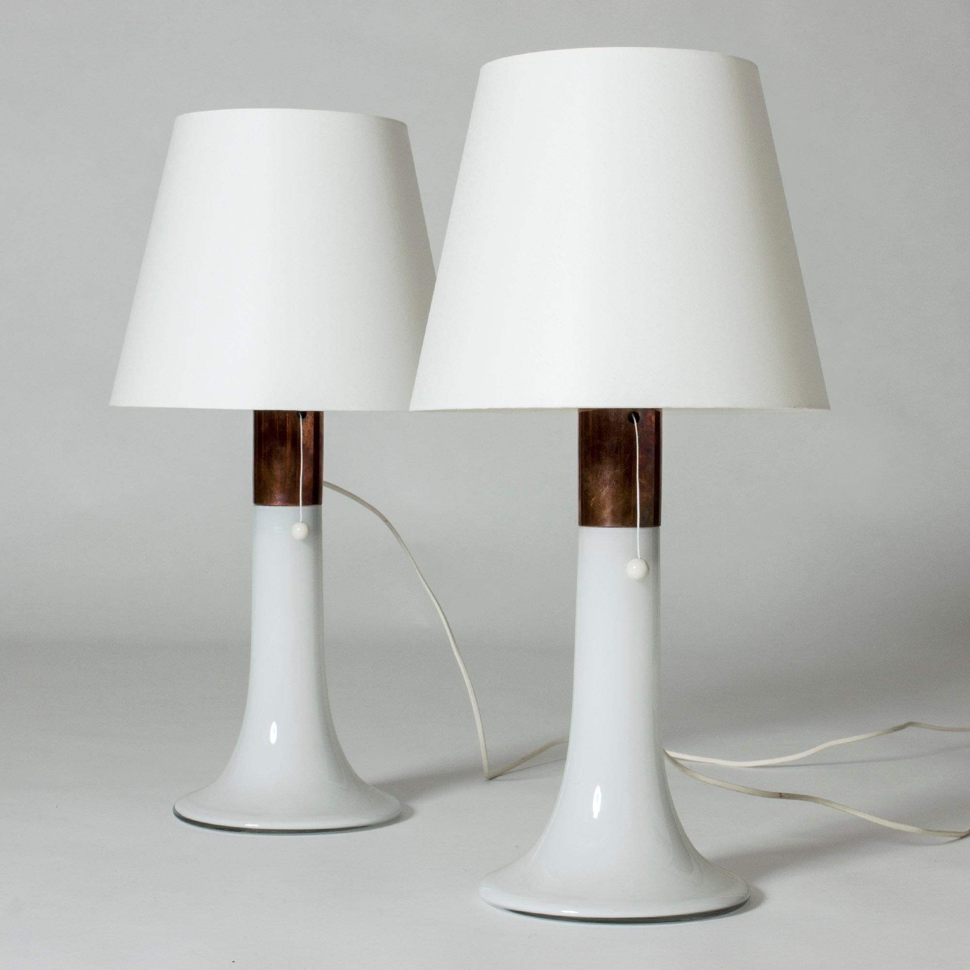 Pair of table lamps in a smooth, streamlined design by Lisa Johansson-Pape. Made from opaque white glass, with a copper rim around the top of the bases.