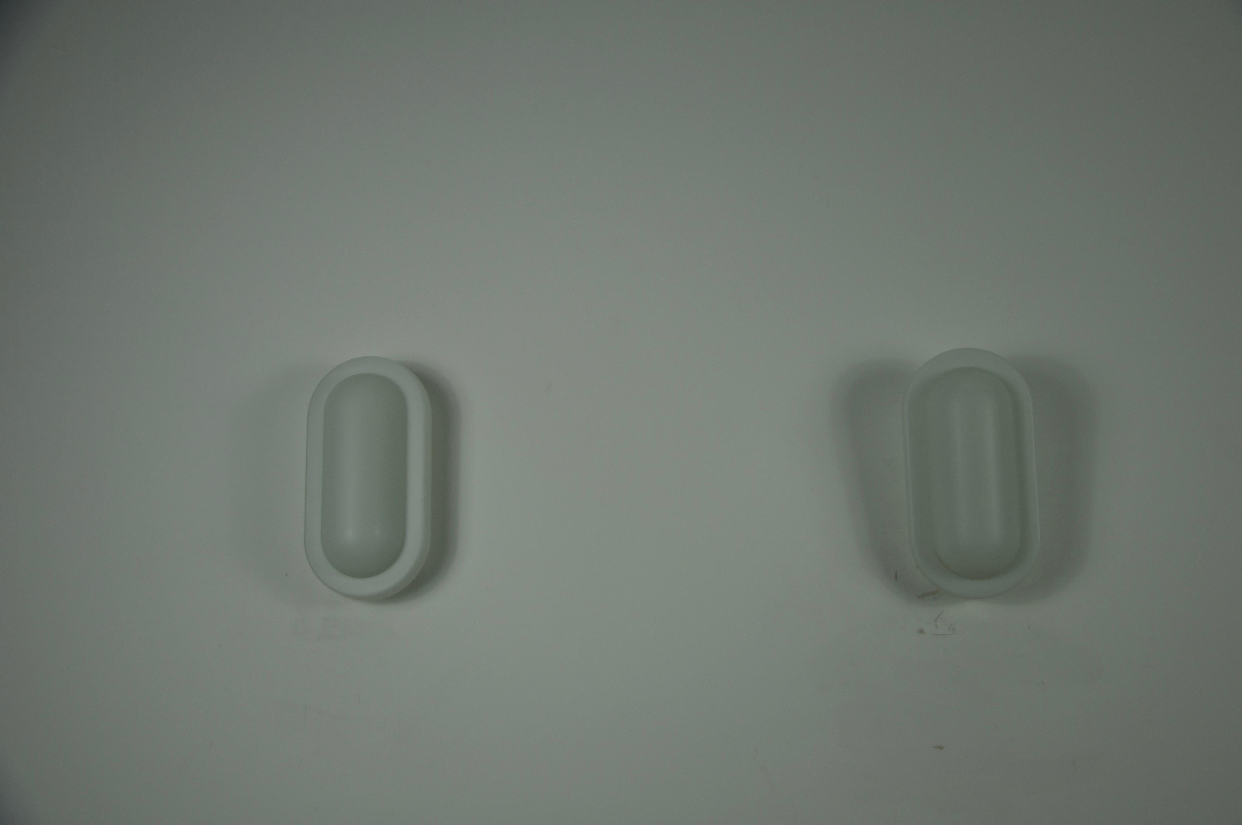 Questa coppia di lampade da parete in vetro è stata progettata da Peill & Putzler in Germania negli anni Settanta. Caratterizzate da una forma minimalista a capsula, le lampade sono realizzate in vetro opalino opaco che diffonde la luce in modo