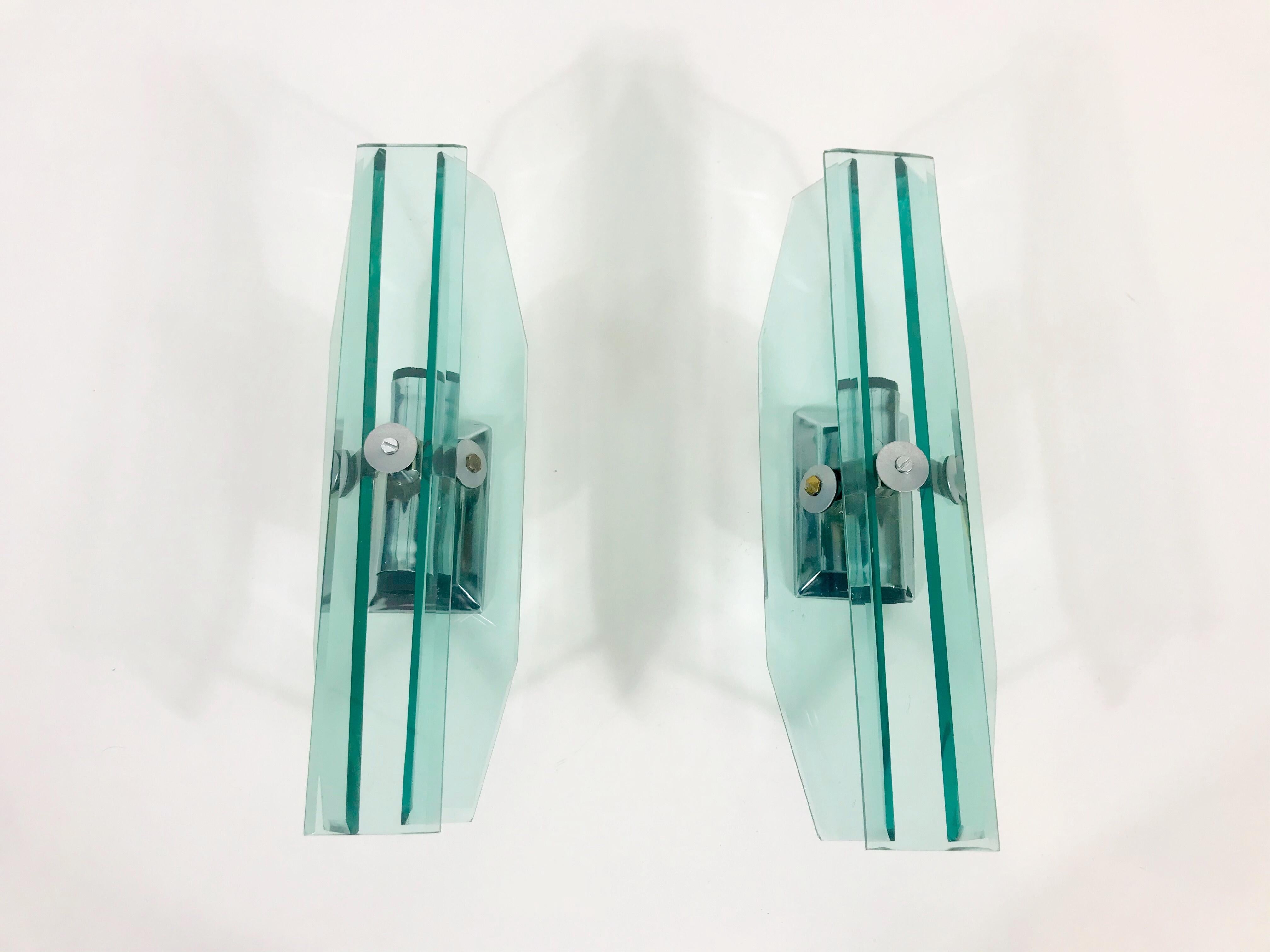 A beautiful pair of glass wall lamps made in Italy in the 1970s. The light is made of thick glass. It has an amazing transparent color and it is very solid. The three glass parts are secure to the body with aluminium and brass screws. The lights