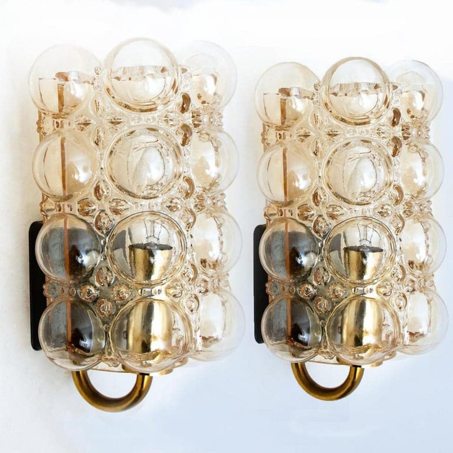Paire de magnifiques appliques en verre bullé conçues par Helena Tynell pour Glashütte Limburg. Un classique du design, le verre soufflé à la main de couleur ambre ou tonique donne une lueur merveilleuse et chaleureuse.xa0

De grande qualité et en
