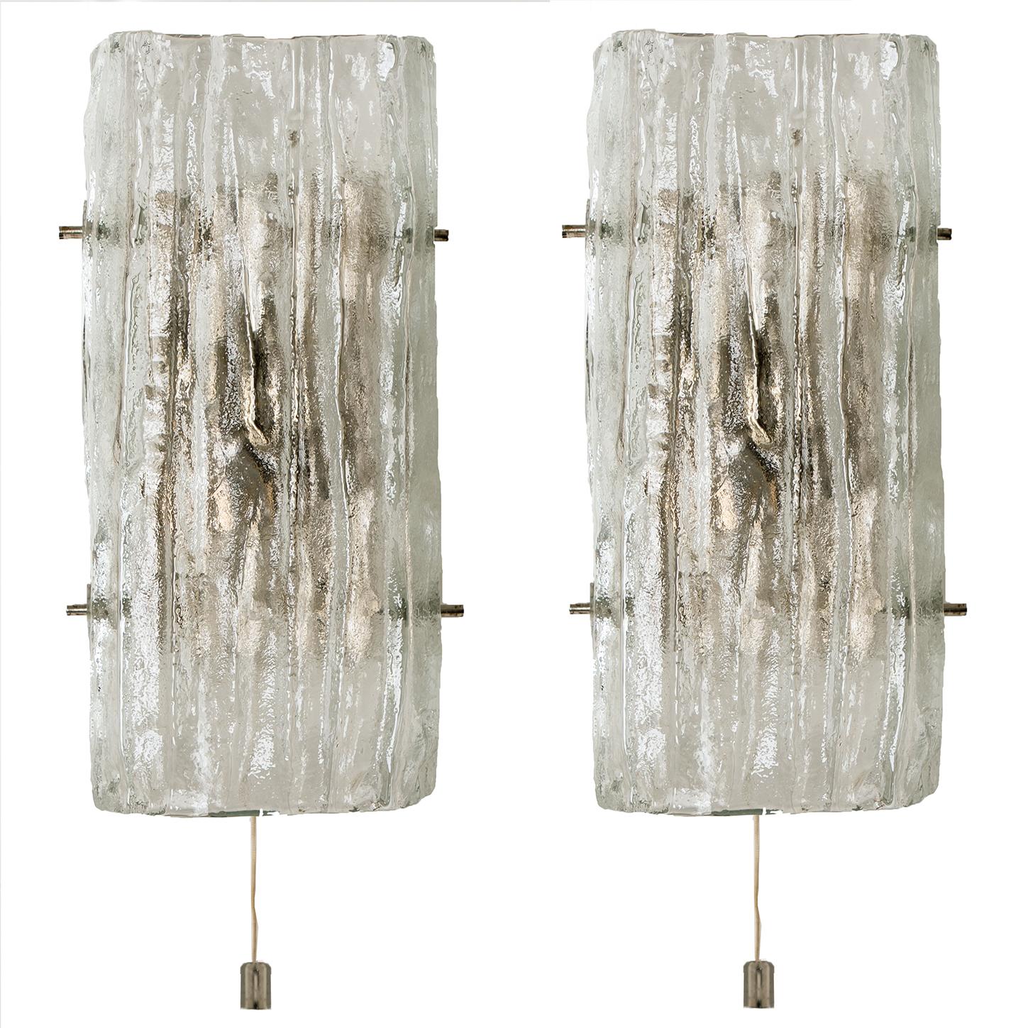 A set of two glass sconces model by Kalmar,Vienna Austria. Manufactured in circa 1970.They are made of a silver painted metal backplate which holds a textured and frosted glass lampshade.

The sconces have a pull-string (on and off) on the bottom
