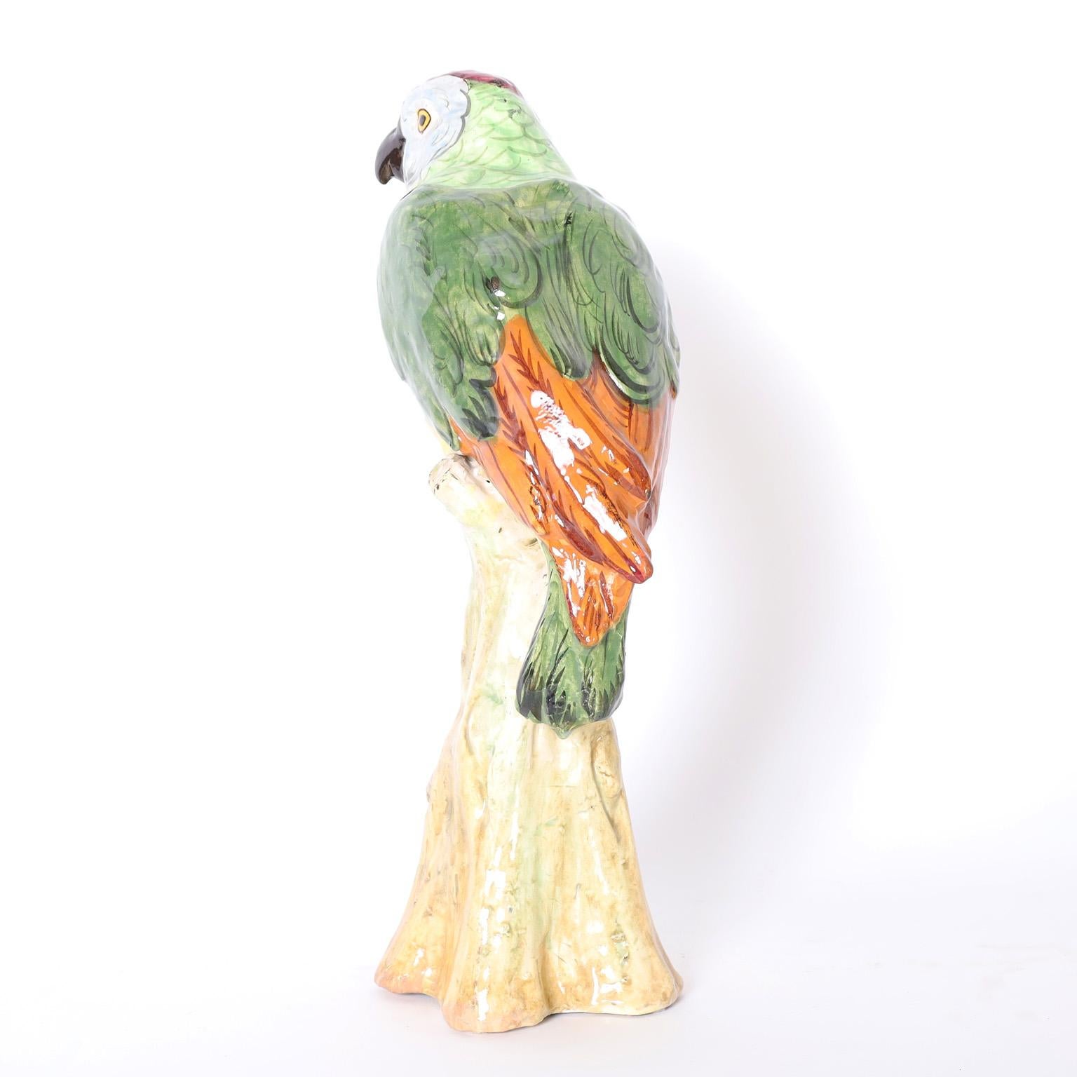 Ein Paar Papageien aus Terrakotta, verziert in tropischen Farben und glasiert, während sie auf künstlichen Baumstämmen hocken.