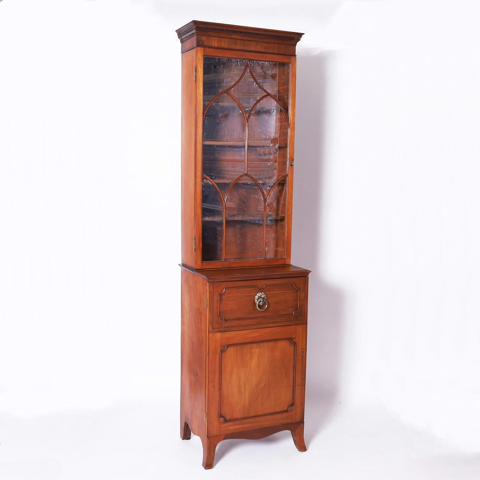 Rare and remarkable pair of British colonial cabinets hand crafted in mahogany and featuring bonnets with carved cornices, glazed step-back bookcases with graceful window pane designs above storage cabinets on Georgian style splayed feet.