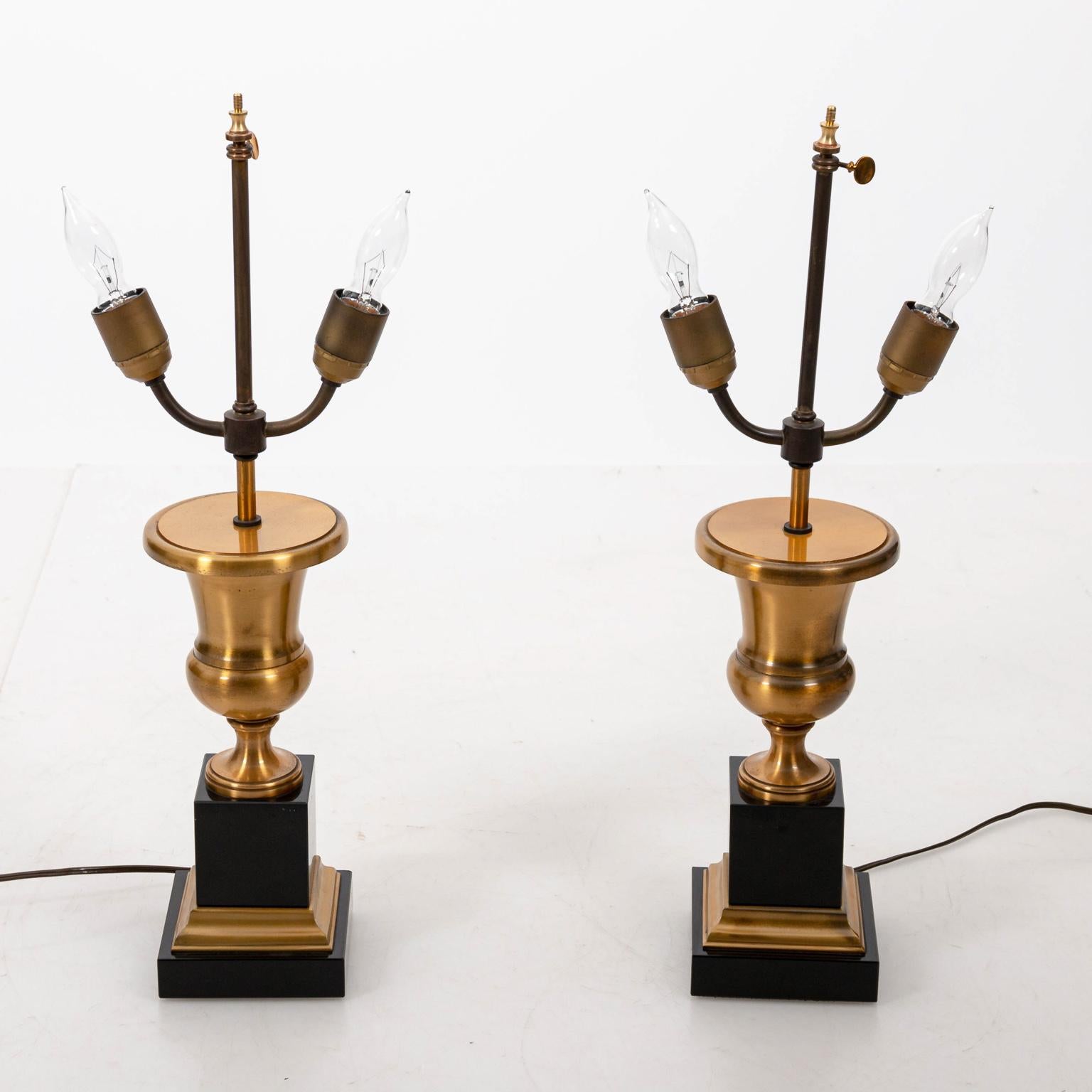 Regency style gold metal urn shaped table lamps on black and gold marble plinth bases, circa 1980s. Made in England. Please note of wear consistent with age.