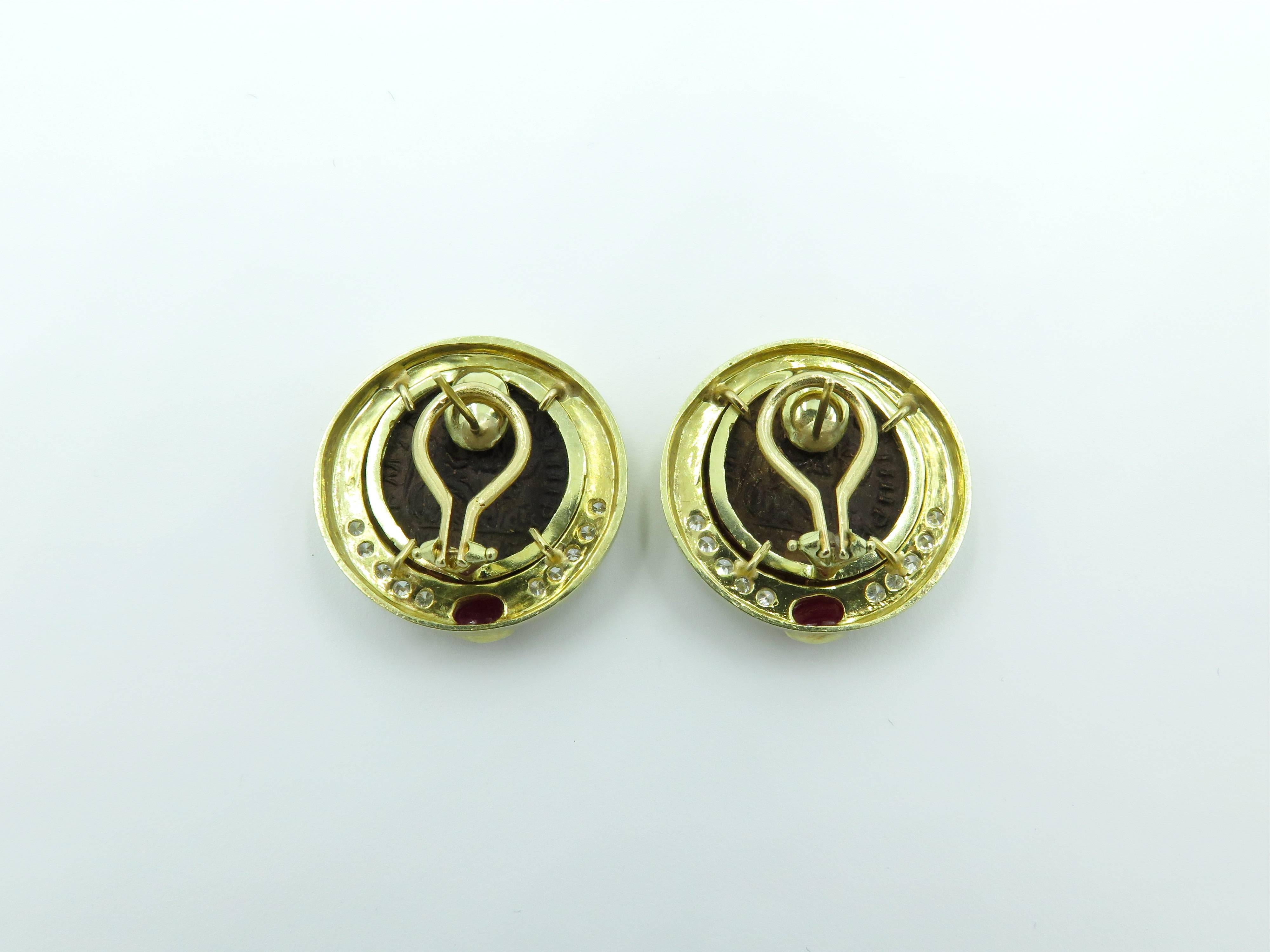 A pair of 14 karat yellow gold bronze coin, diamond and cabochon ruby earrings. Each designed as polished gold circular plaque, set with a bronze depicting a classical  man in profile, enhanced by circular cut diamonds and an oval cabochon ruby.