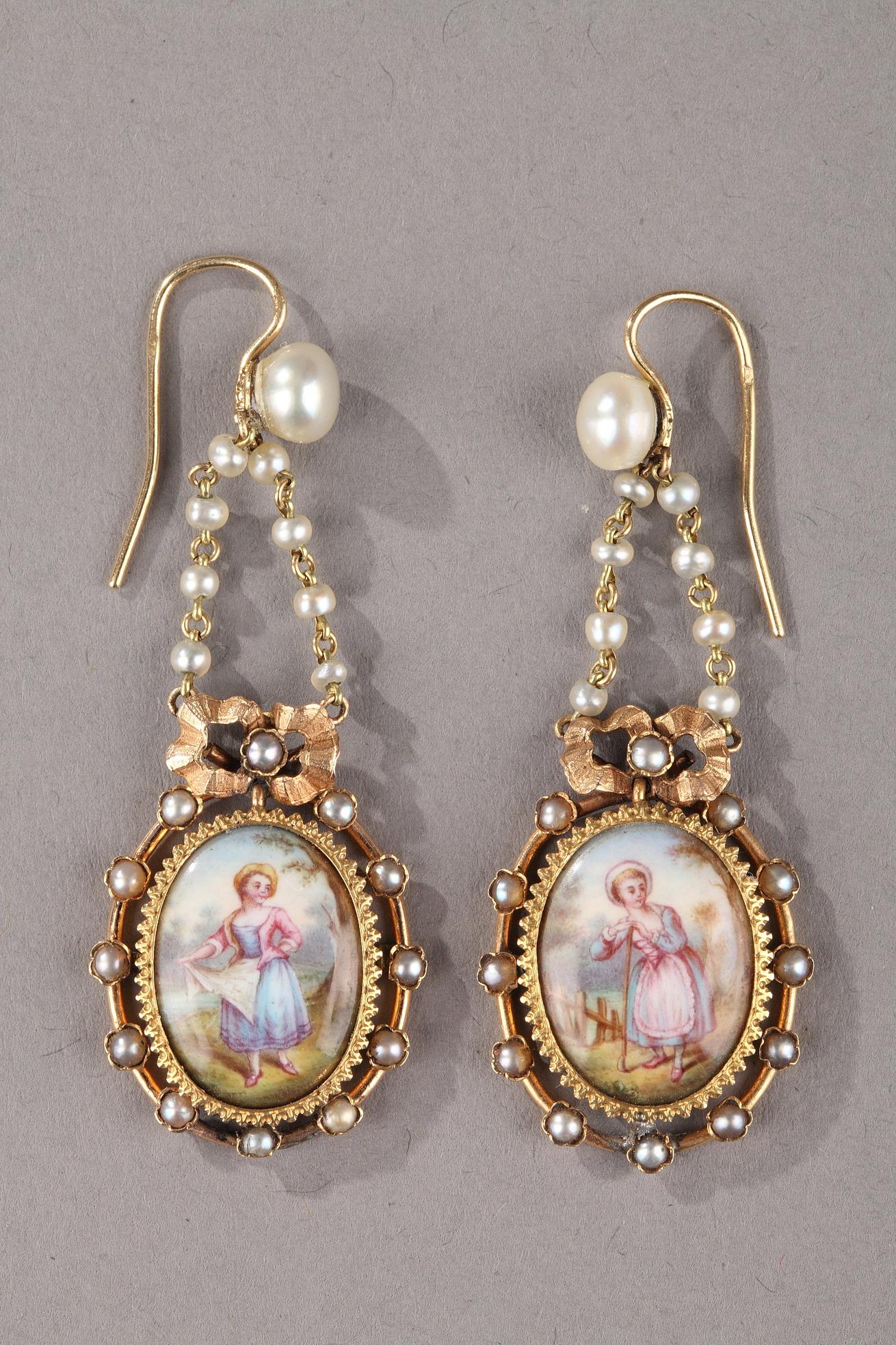 Pair of gold earrings. The pendant of each earring is suspended by alternating pearls and gold beads. Enamel medallions set in a gold mounting embellish the earrings. The mounting itself is set with pearls and topped with a bow. The miniatures