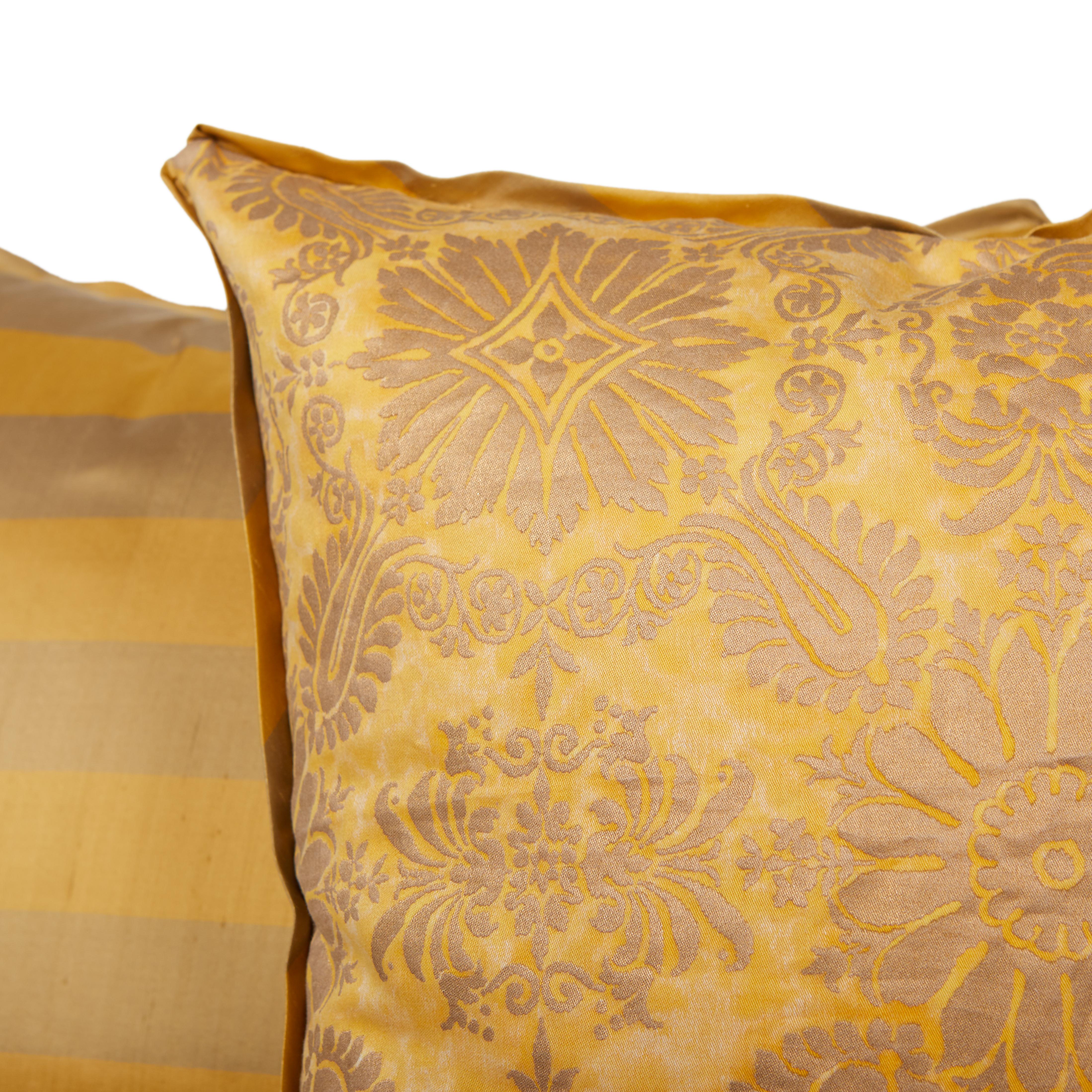 A pair of Fortuny fabric cushion in the Impero pattern, featuring a gold and beige colorway. Exquisite details including a lovely striped silk backing material and golt silk edging. The Impero pattern is a 19th century French design with formal
