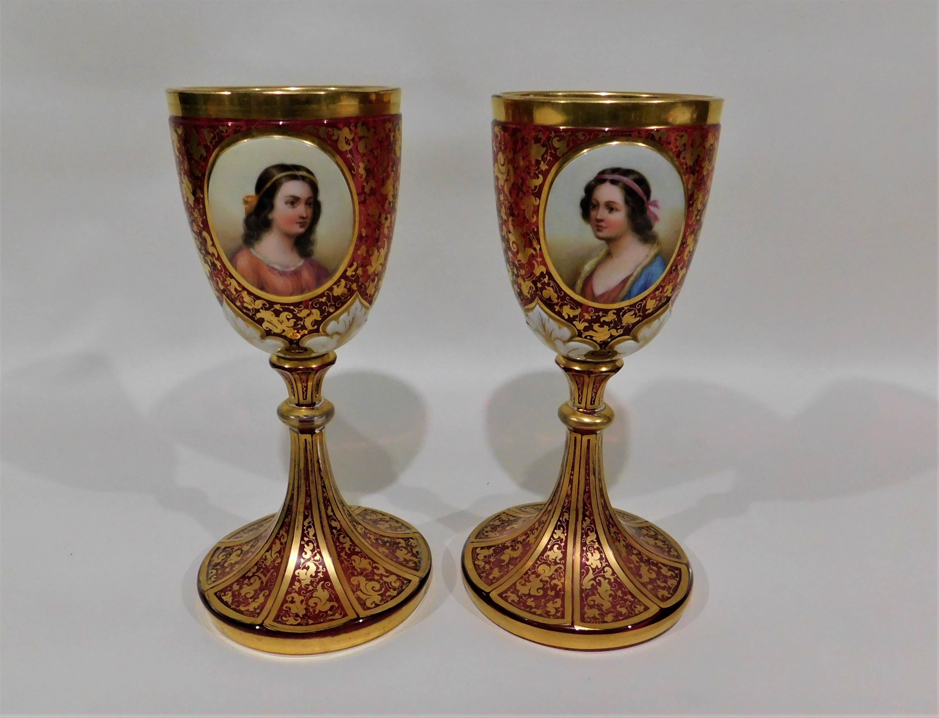 19th century pair of gold gilt hand-painted Bohemian ruby red glass enameled goblets. Portraits of women and flowers within cartouches, with foliage and floral designs throughout.