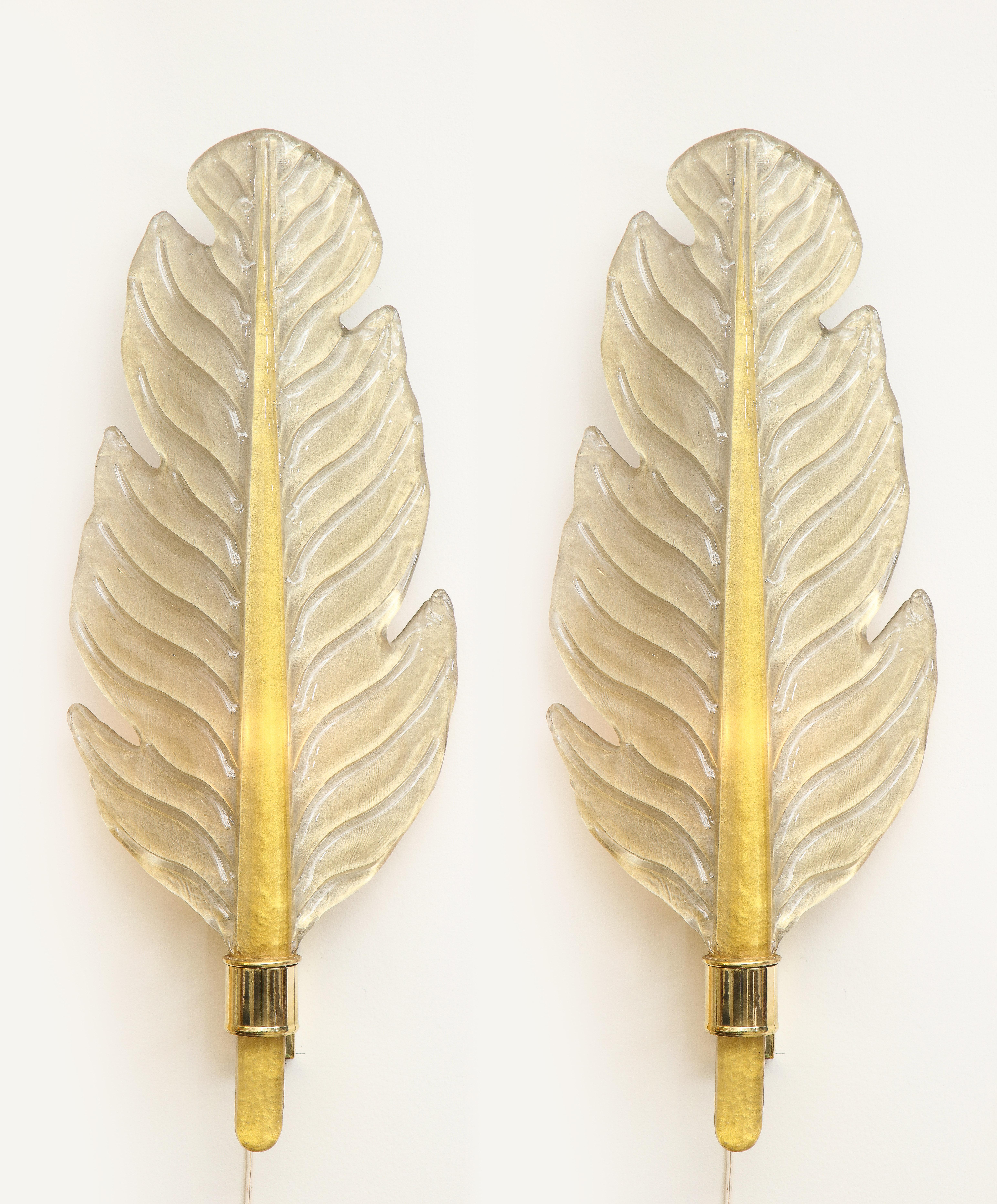 Pair of handcasted clear Murano glass sconces infused with 24-karat gold to give the glass a metallic, shimmering effect. The solft shimmering gold leaf is accentuated by the deeper gold center stem. This pair of leaf-shaped sconces were
