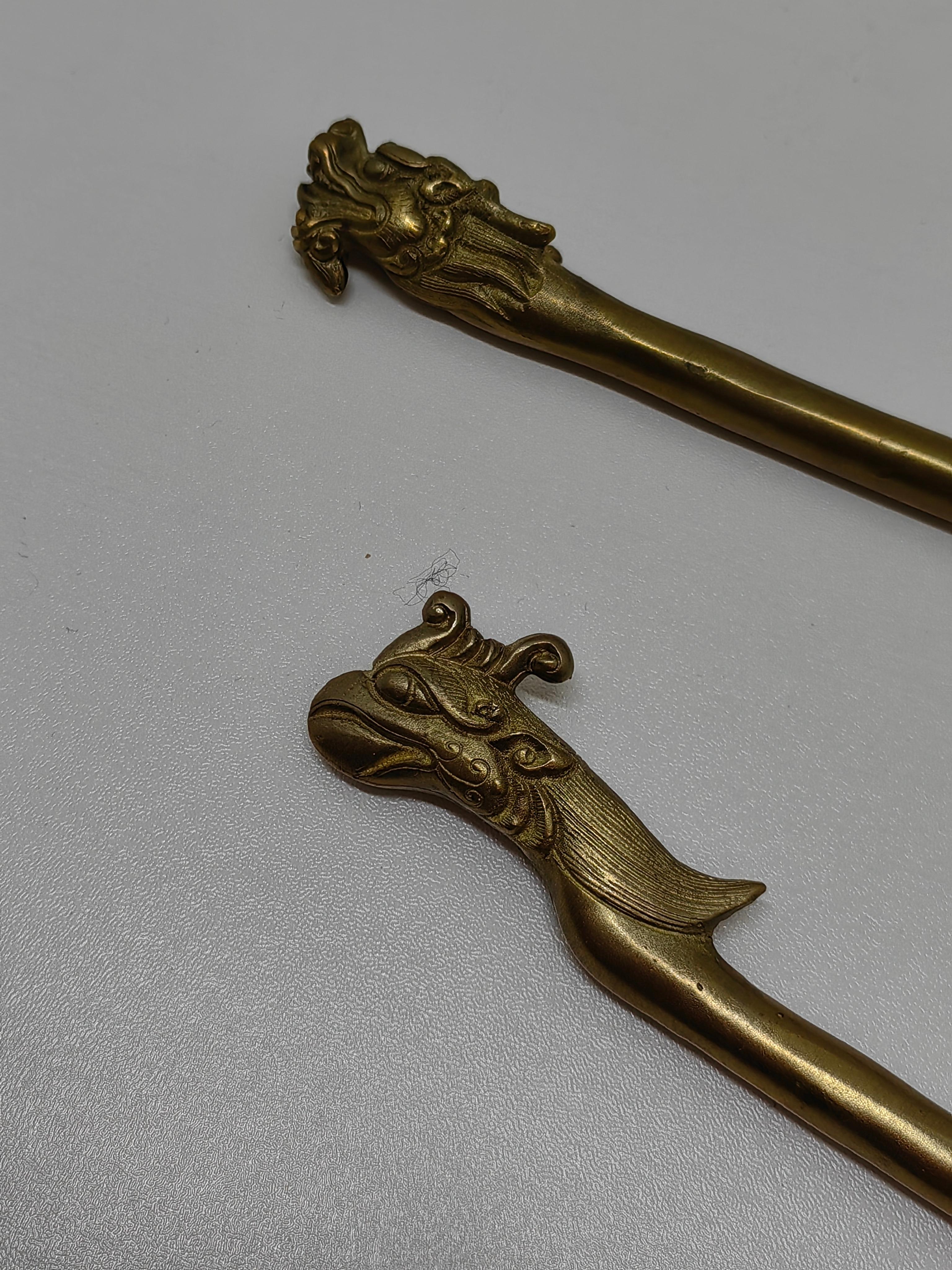 Embrassez la beauté et le symbolisme de la culture chinoise traditionnelle avec cette superbe paire d'épingles à cheveux en métal doré représentant les emblématiques dragon et phénix. Ces élégants accessoires de coiffure allient un savoir-faire