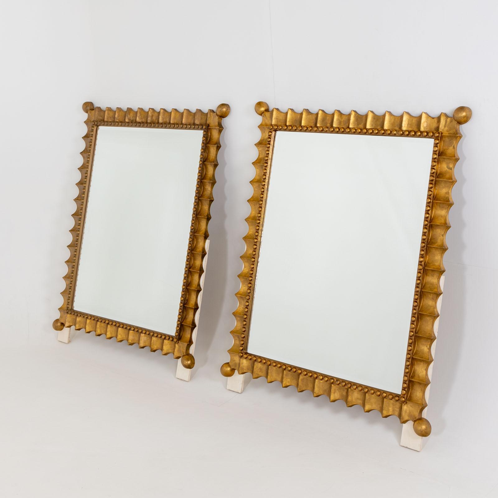 Grande paire de miroirs muraux festonnés et patinés or, milieu du 20e siècle. Ces miroirs muraux impressionnants sont dotés d'un cadre patiné or et d'un bord ondulé distinctif orné d'une décoration perlée. Les angles se terminent élégamment par des