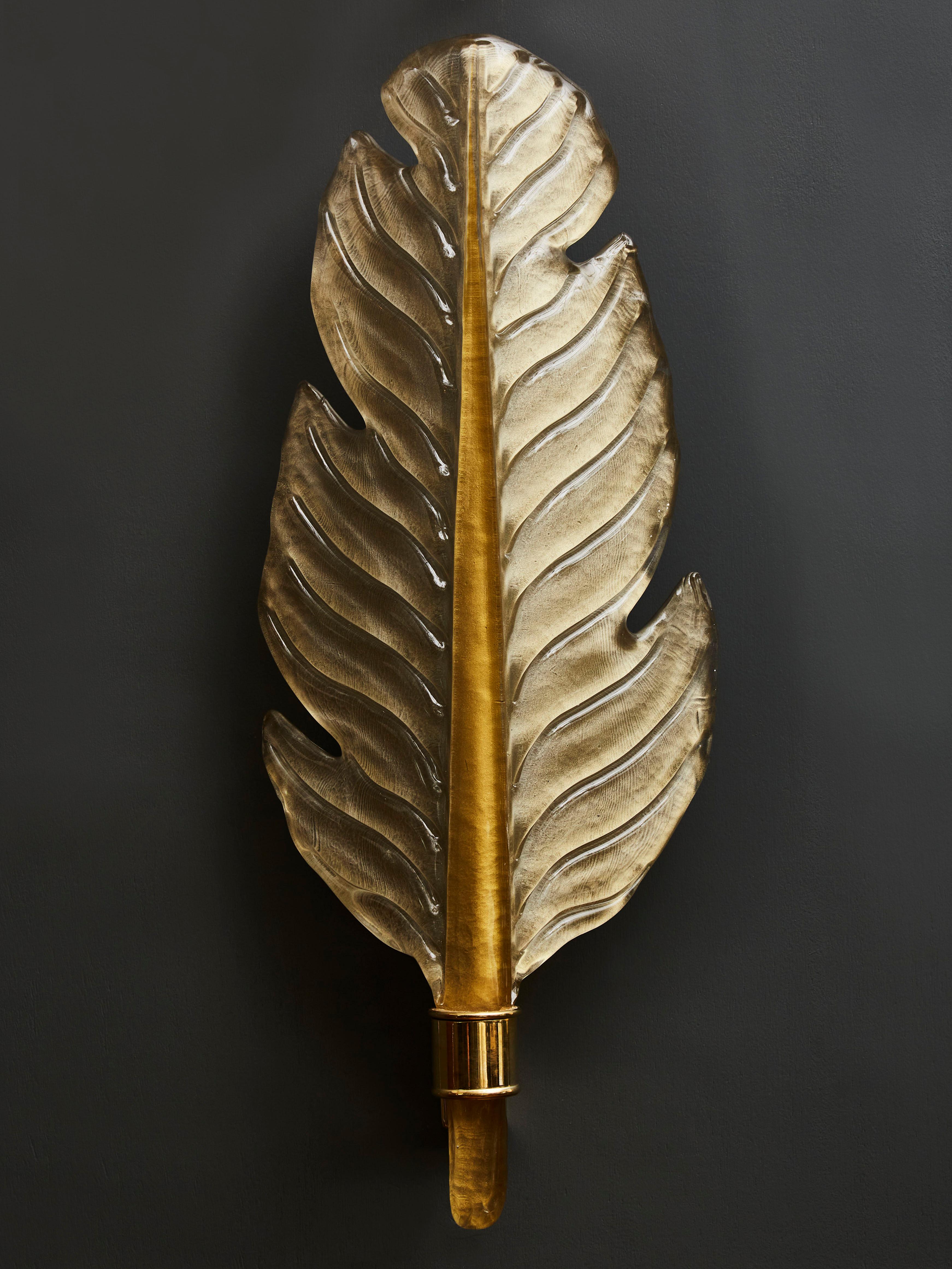 Pair of wall sconces made of tinted Murano glass and shaped like big leaves. Brass setting at the stem, holding one light per sconce.