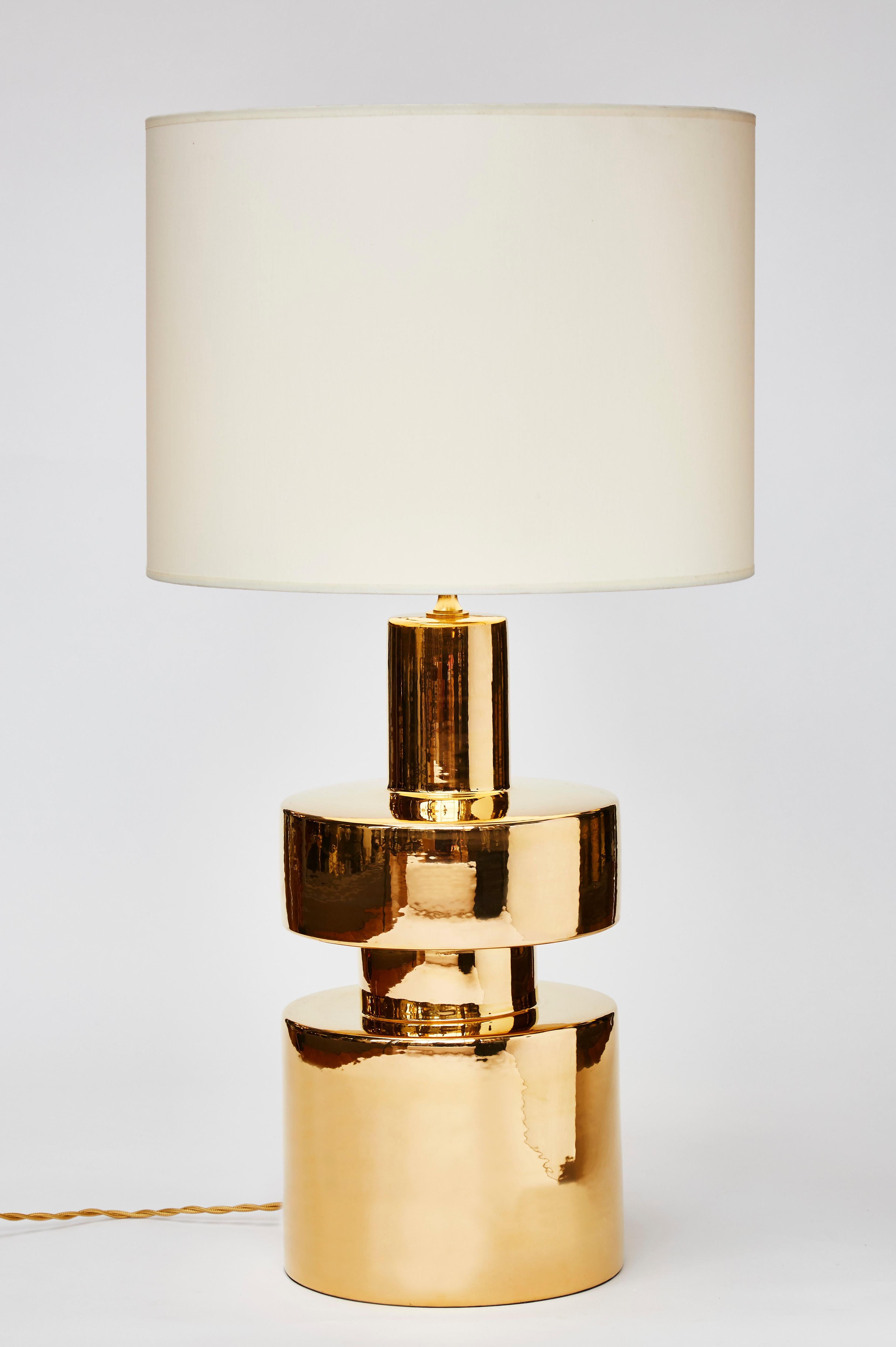 Pair of cylindrical table lamps made of ceramic covered with a golden glaze reflecting the light.