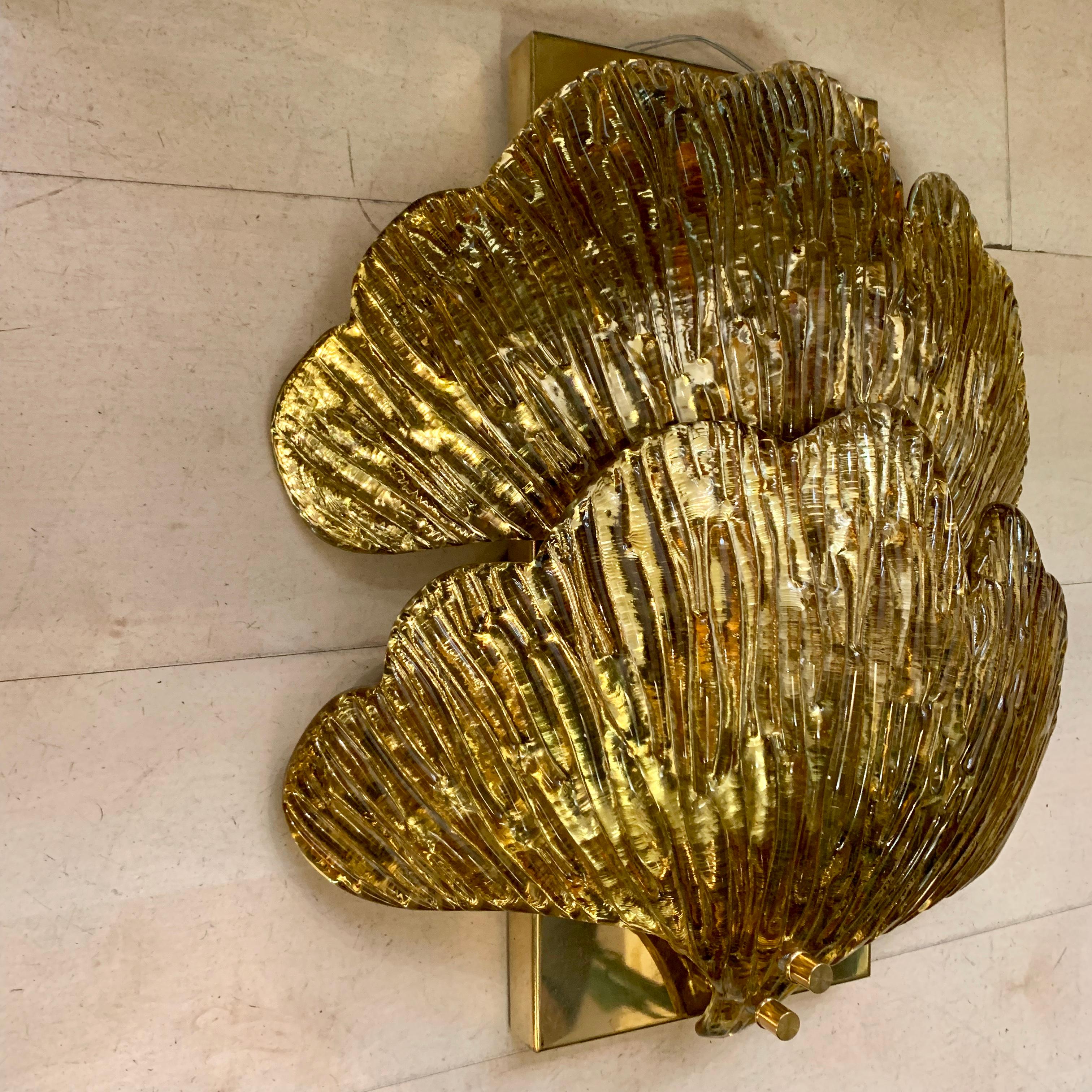 Pair of golden Murano glass mirrored ginkgo leaf sconces.
Each applique is composed of two gilded ginkgo leaves in mirrored hand blown Murano glass.
The structure is in brass and there are 4 bulbs per sconces.