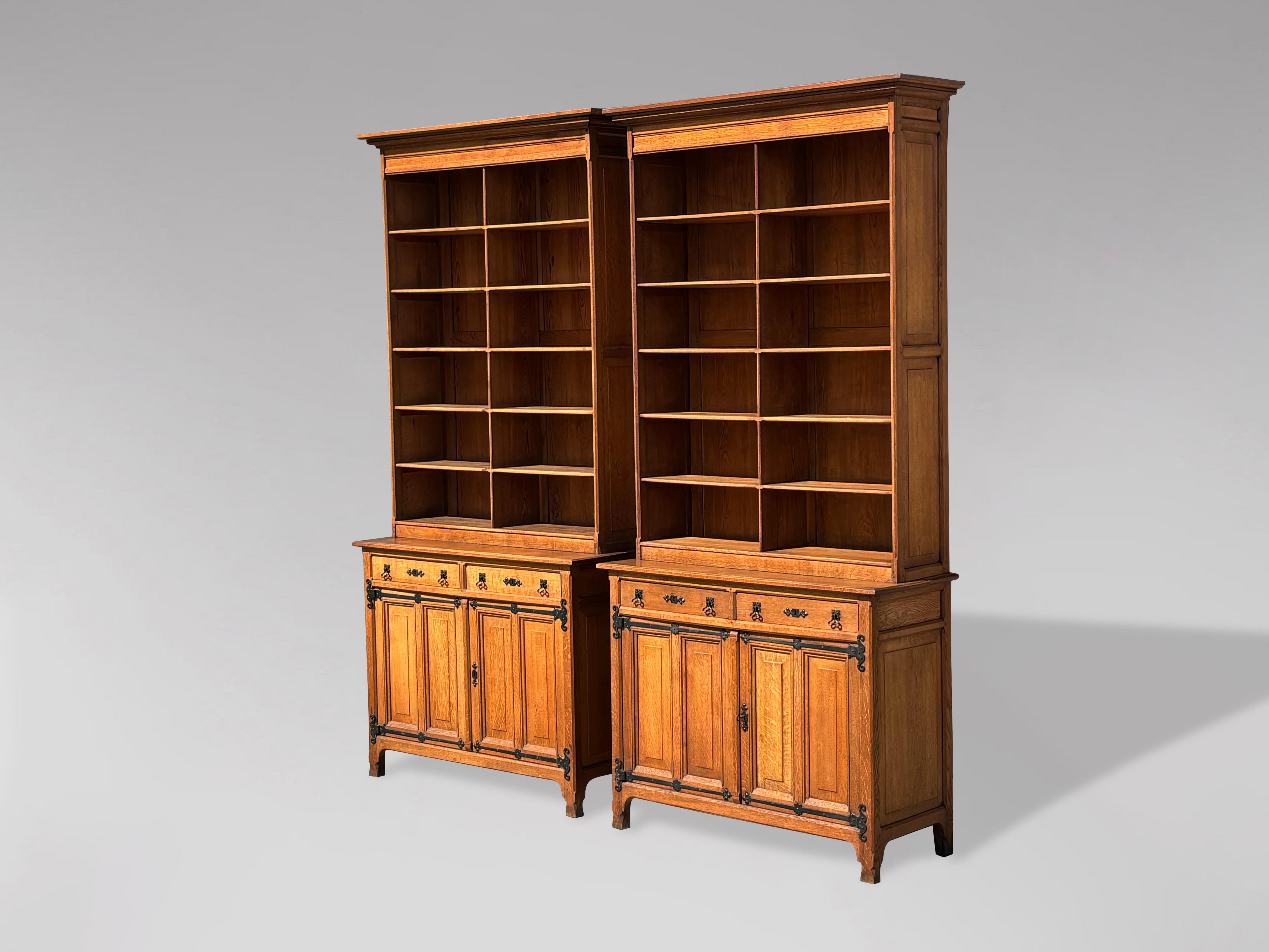 A high-quality pair of golden oak Arts & Crafts library bookcases. The moulded cornice sits above an open bookcase with ten fixed, moulded, detailed, and shaped shelves. The lower section features two drawers with well-shaped iron handles and two