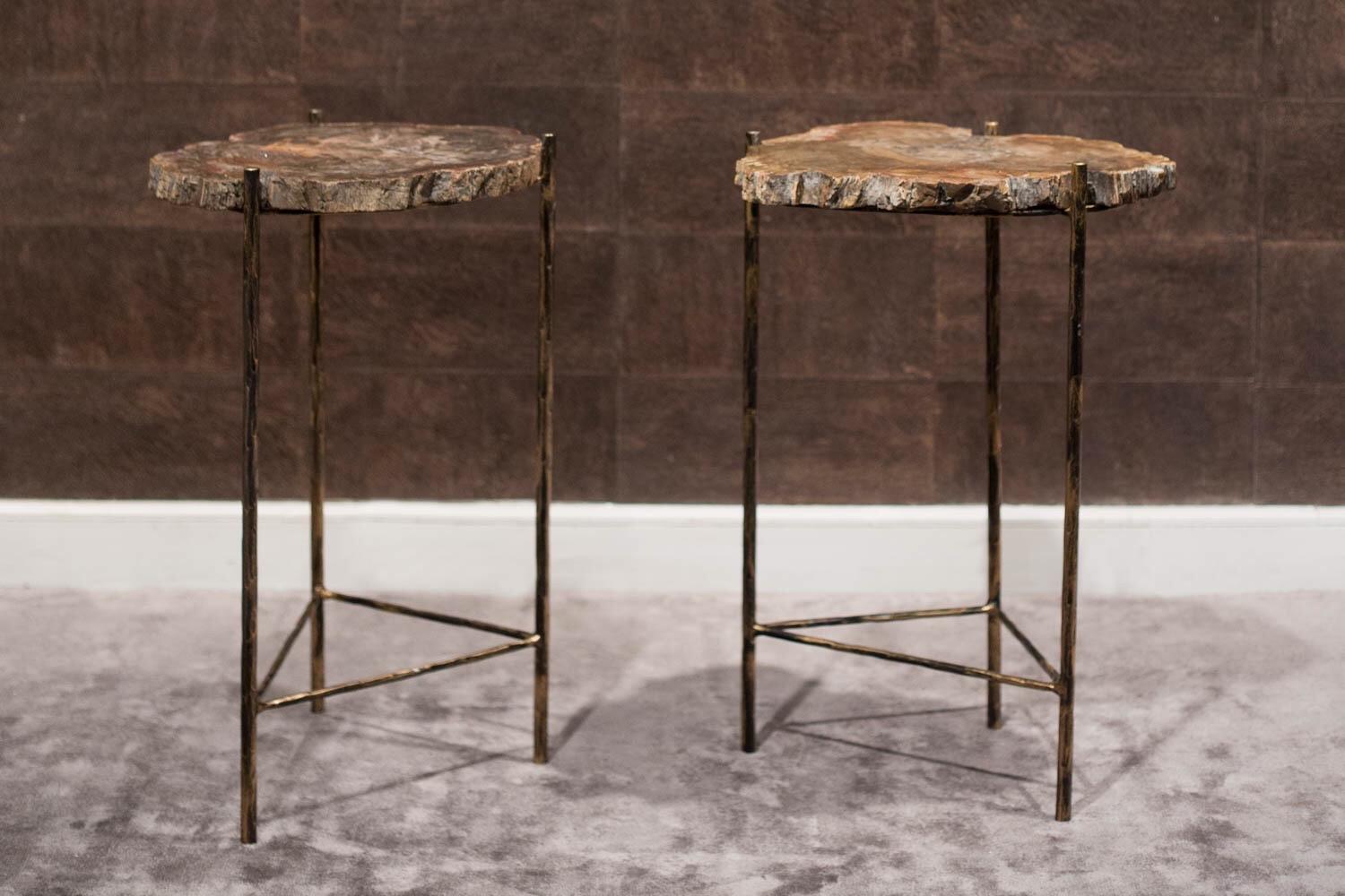 The two tabletops are made of two wonderfully unique, irregular pieces of veined fossil wood, supported on a three-foot base in black iron with golden highlights. In the lower part, the legs are joined together by a triangular piece, also black iron