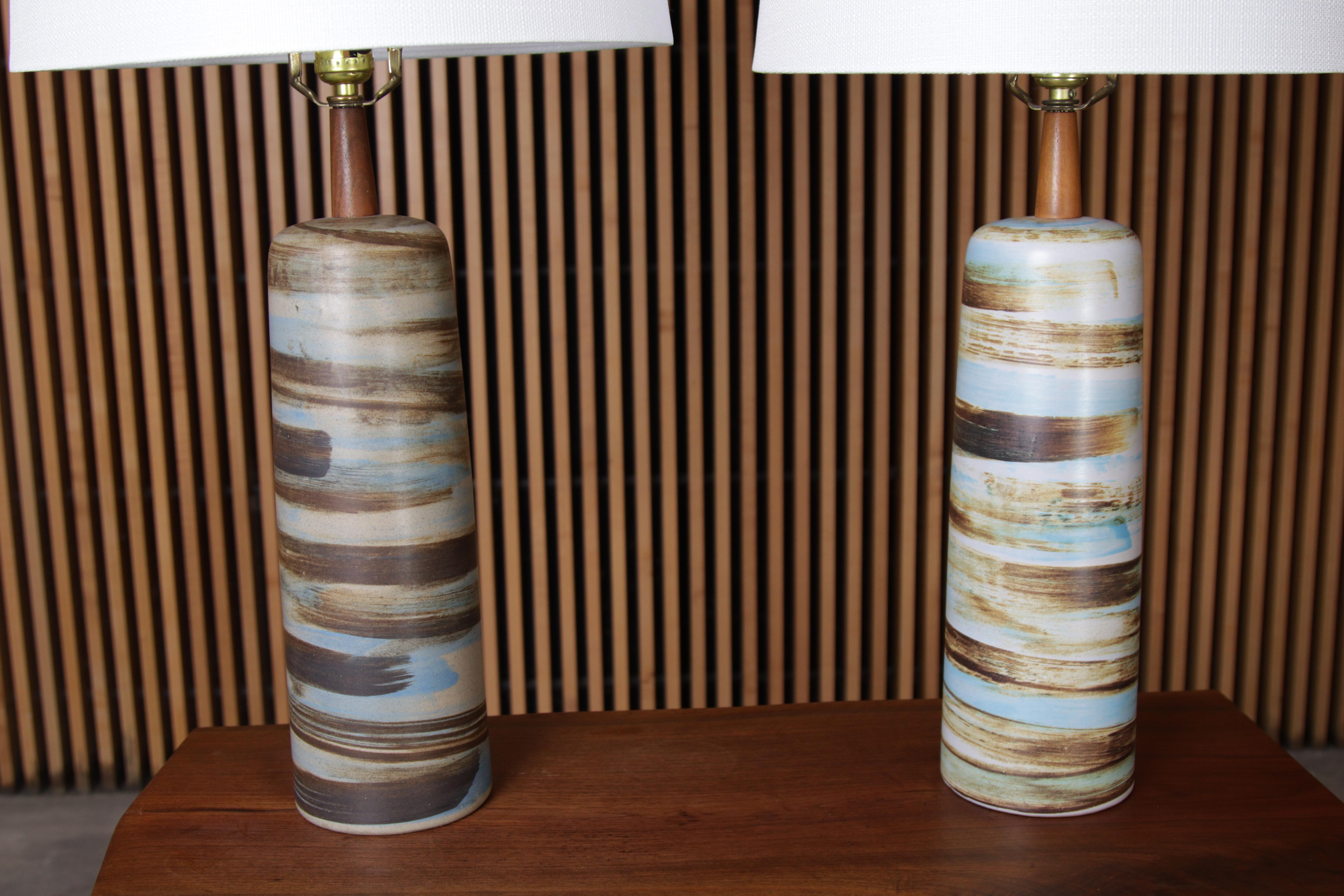 A pair of ceramic and walnut lamps designed by Jane and Gordon Martz for Marshall Studios. Ceramic glaze featuring light blue, white, tan and brown swirls. Every lamp is handmade, glazed and unique. One lamp shows a darker glaze and one shows a