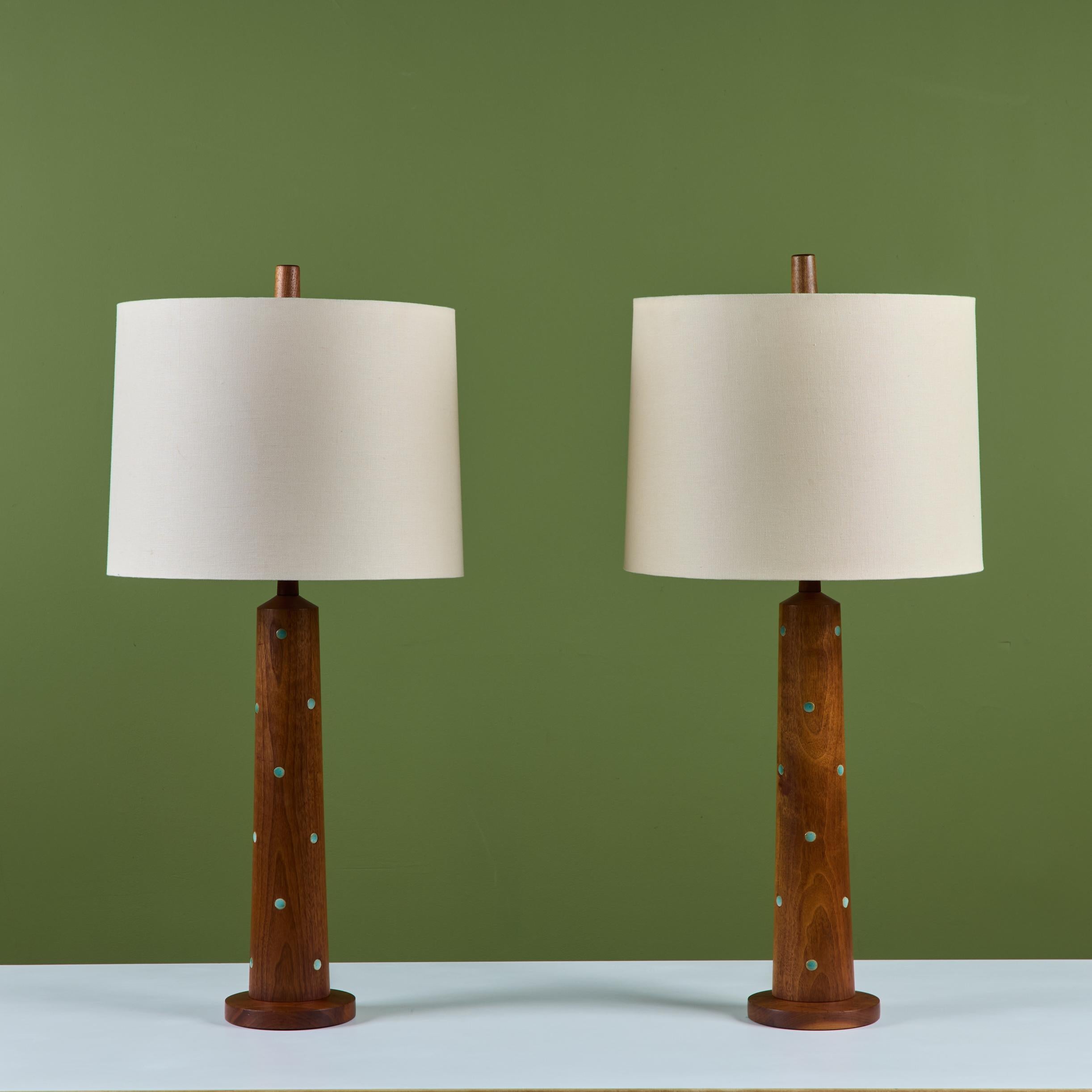 Coppia di lampade in noce tornite dagli artisti ceramisti del Midwest Gordon & Jane Martz per la loro azienda Marshall Studios. Le lampade da tavolo hanno una leggera forma a clessidra e sono intarsiate con piccole piastrelle di ceramica con monete