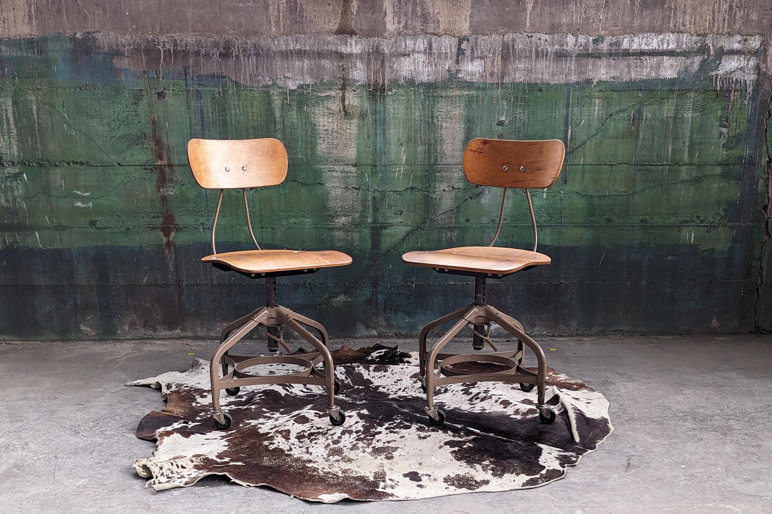 A PAIR of 2 Toledo Metal Furniture Co. chairs from the mid 20th century that can be adjusted for use in drafting, office, or university settings.

These chairs have a bentwood seat and seat back with a beige metal base and are equipped with casters