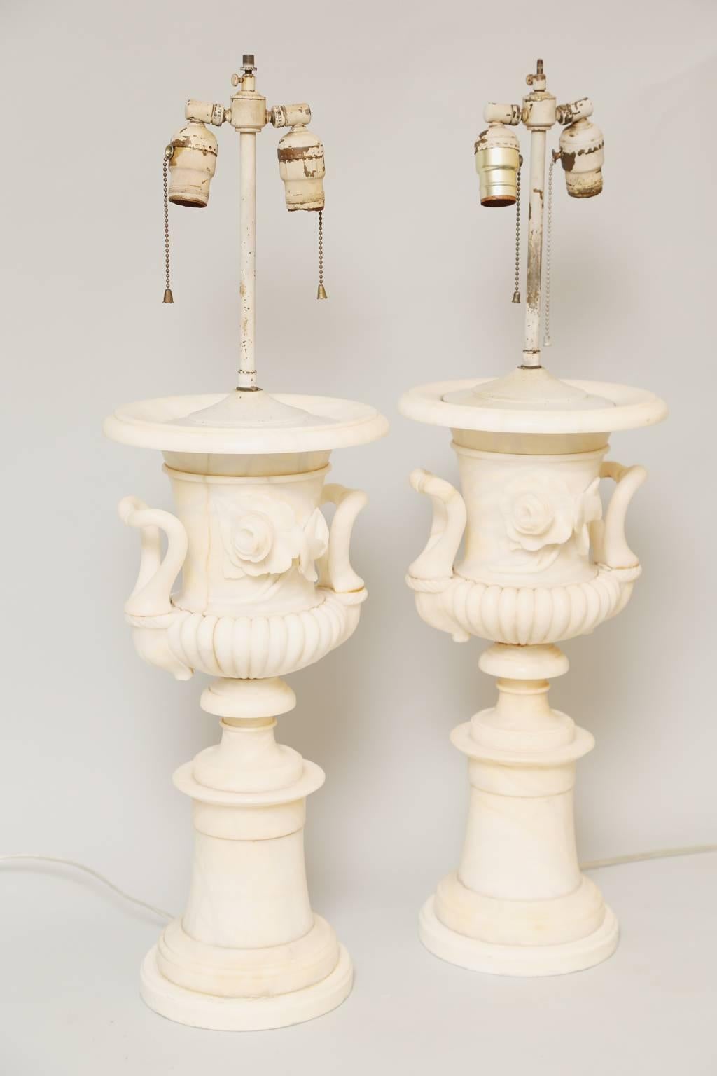 Pair of table lamps, of carved alabaster, each a campana form urn, its body outcarved with blossoms, flanked by curved handles, on fluted socle, raised on round footed base, set upon graduated cylindrical plinth.

Stock id: D1248.