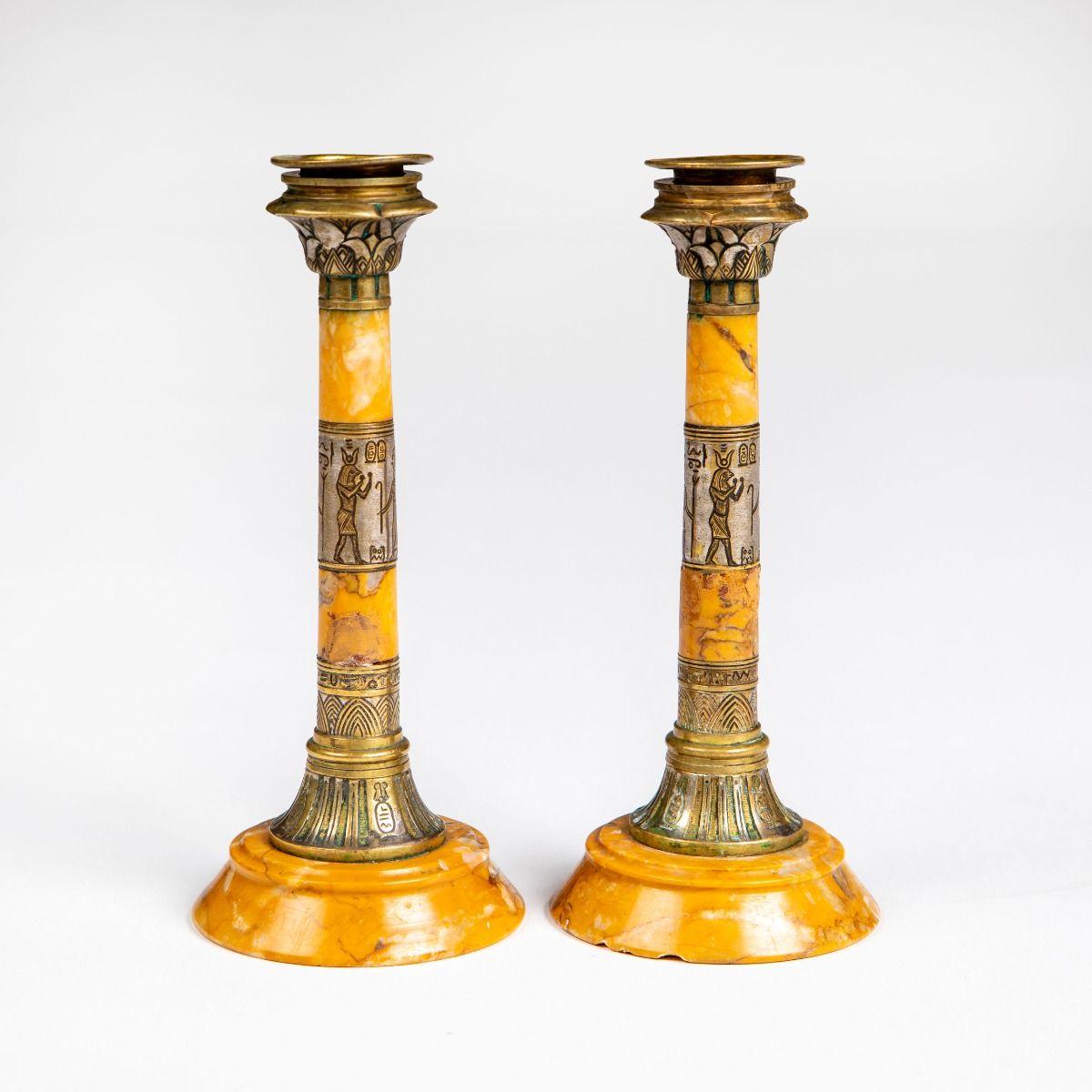 Una coppia di eleganti candelieri Grand Tour realizzati in marmo travertino dorato e riccamente ornati da montature in bronzo patinato.
I gambi presentano fregi egiziani incisi che raffigurano figure e simboli ispirati all'iconografia dell'antico