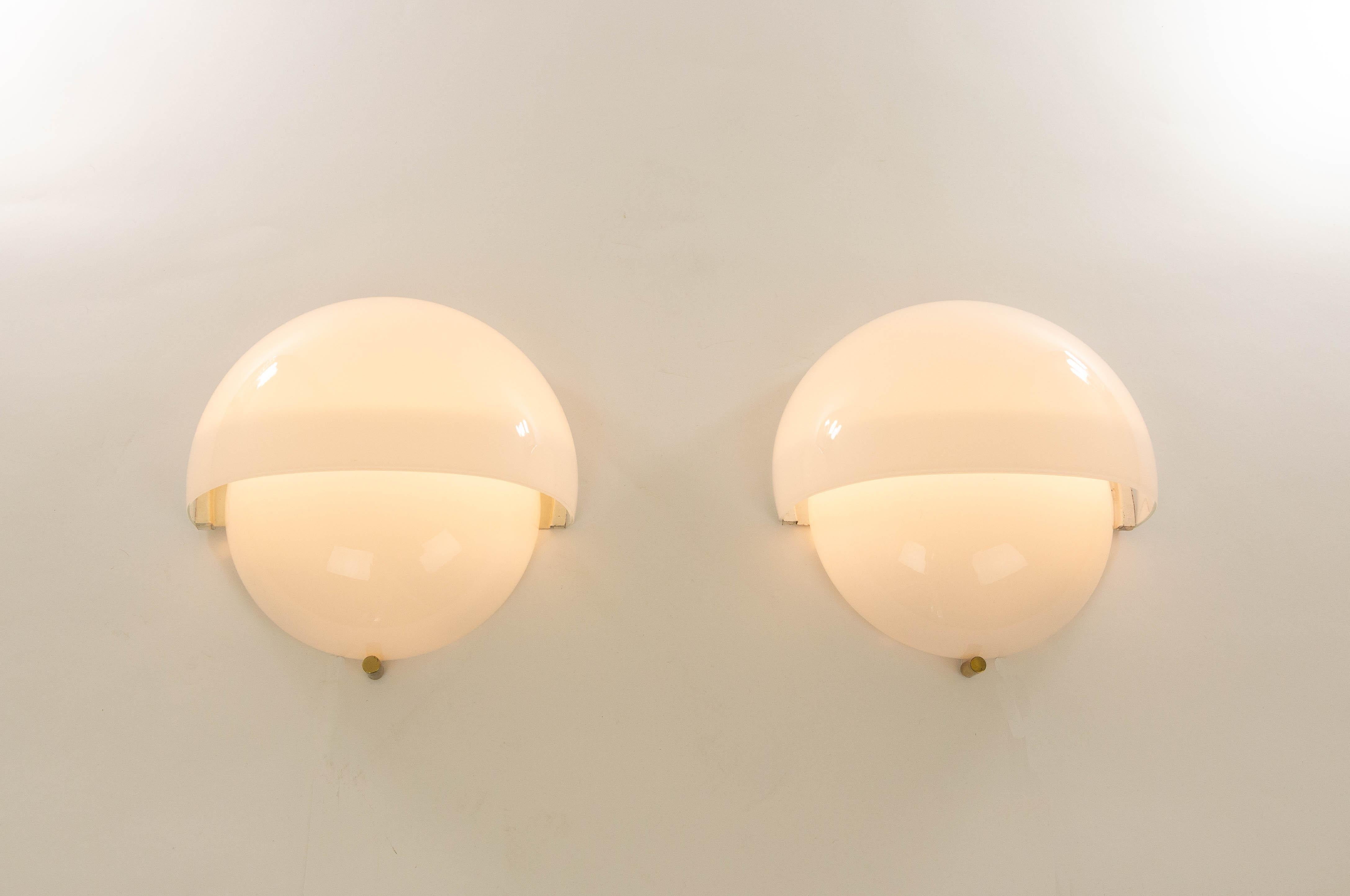 A pair of Grande Mania wall lamps designed by Vico Magistretti and produced by Artemide in 1963.

This is the original version, made of two opaline glass shells and with a very nice brass detail at the bottom of the lamp.

Both lamps are in very