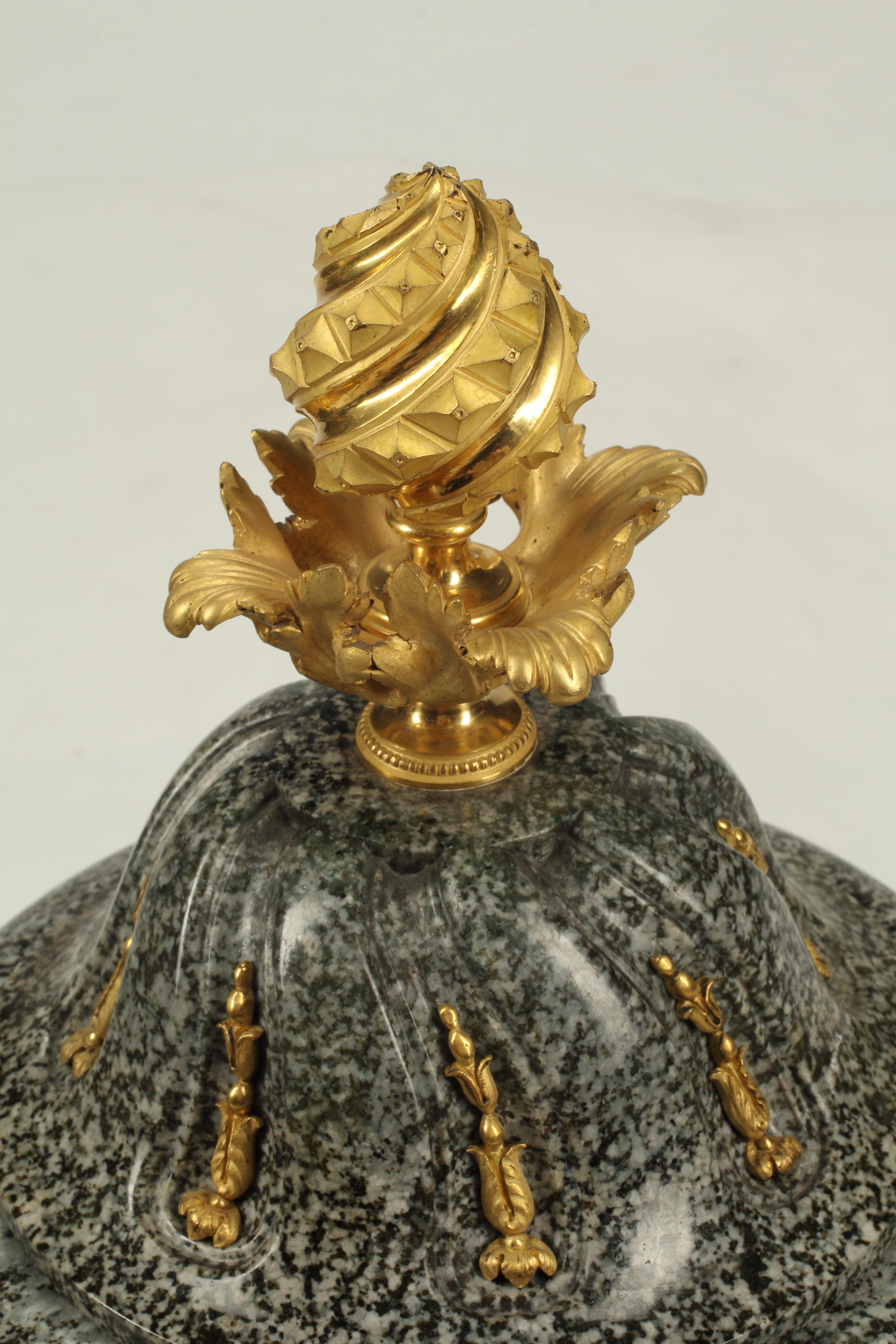 Questa coppia di urne presenta uno straordinario connubio tra la forza del granito e la lussuosa bellezza dei dettagli in bronzo dorato. Queste urne sono intagliate in modo unico con scanalature a spirale che emulano i dettagli architettonici e