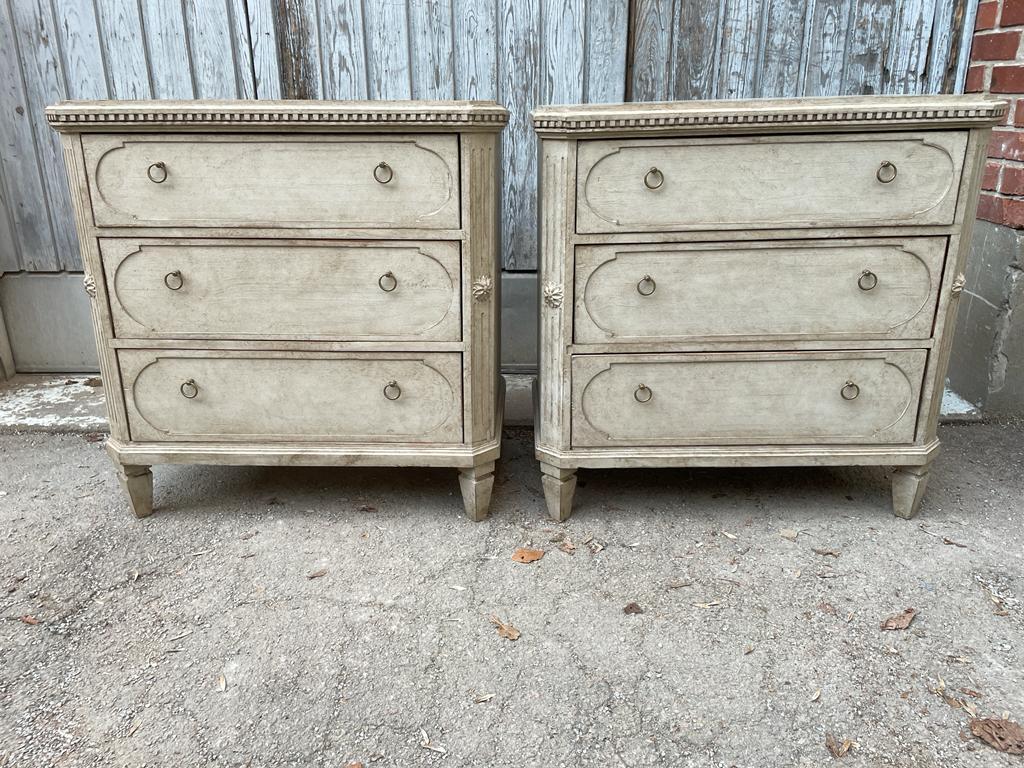 A pair of light gray painted 3 drawer chests with original brass hardware and faux marble table top. The canted corners with carved lion head medallions are typical of the Gustavian period.
 