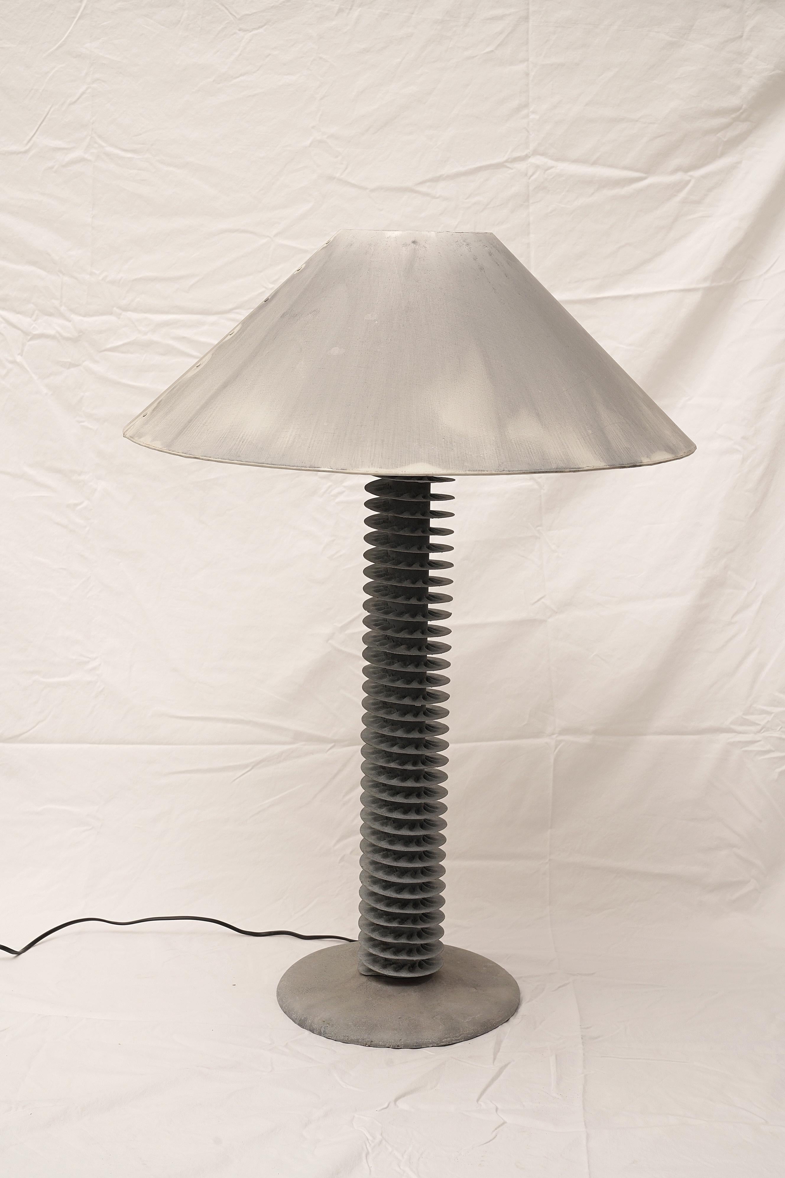 An unusual re-purposing, spiral grey metal water condensers mounted on a cast stone base and stem to make a great pair of table lamps. Gray metal lamp shades with intentional but subtle color variations. American, circa 2000. Shades are 24