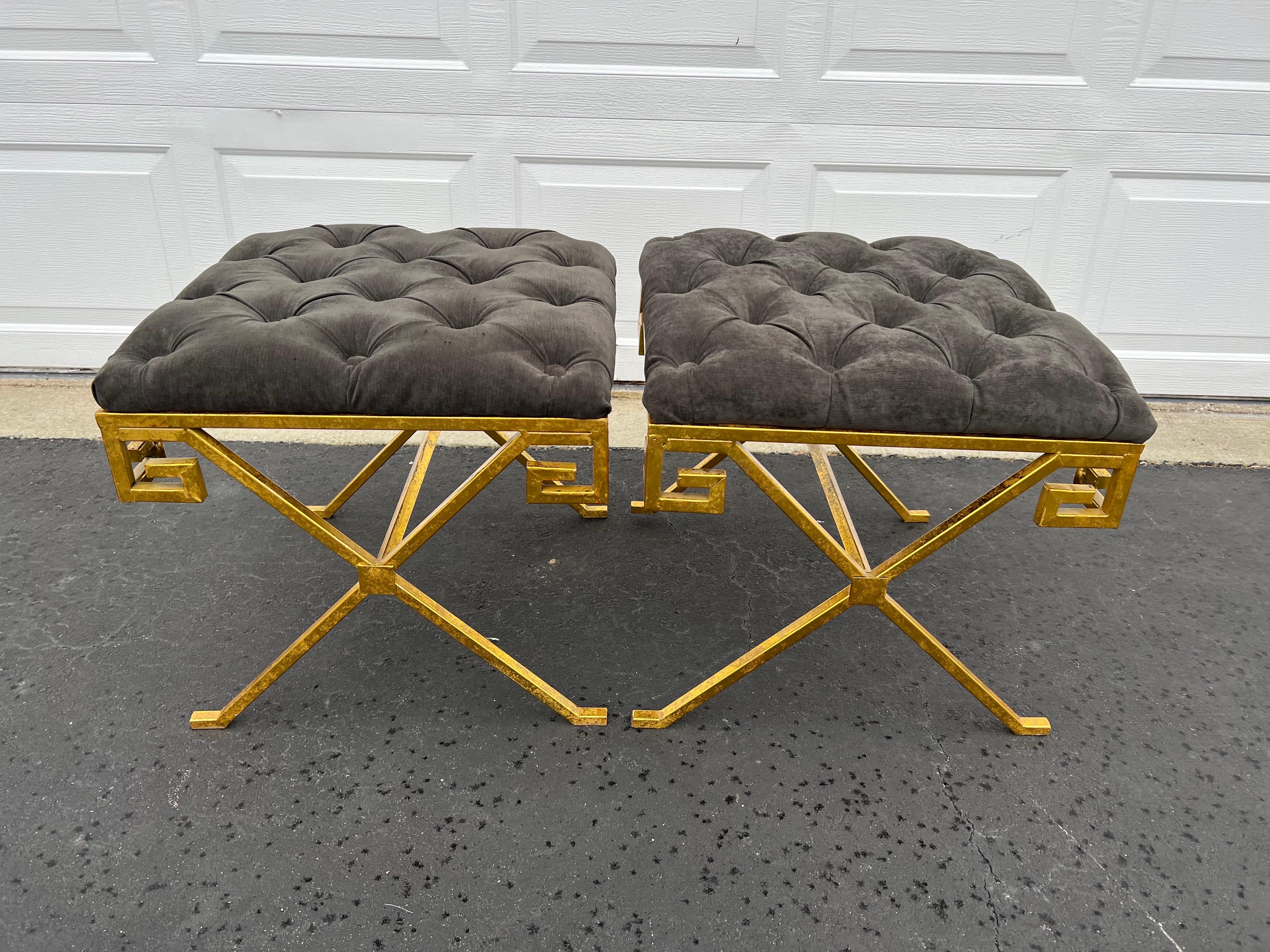 Pair of Greek key tufted gray velvet ottoman stools. These are new but have such a nice decorative appeal. Perfect for at the foot of a bed or under a console. One foot has a padded support as it is a bit shorter than the other legs.