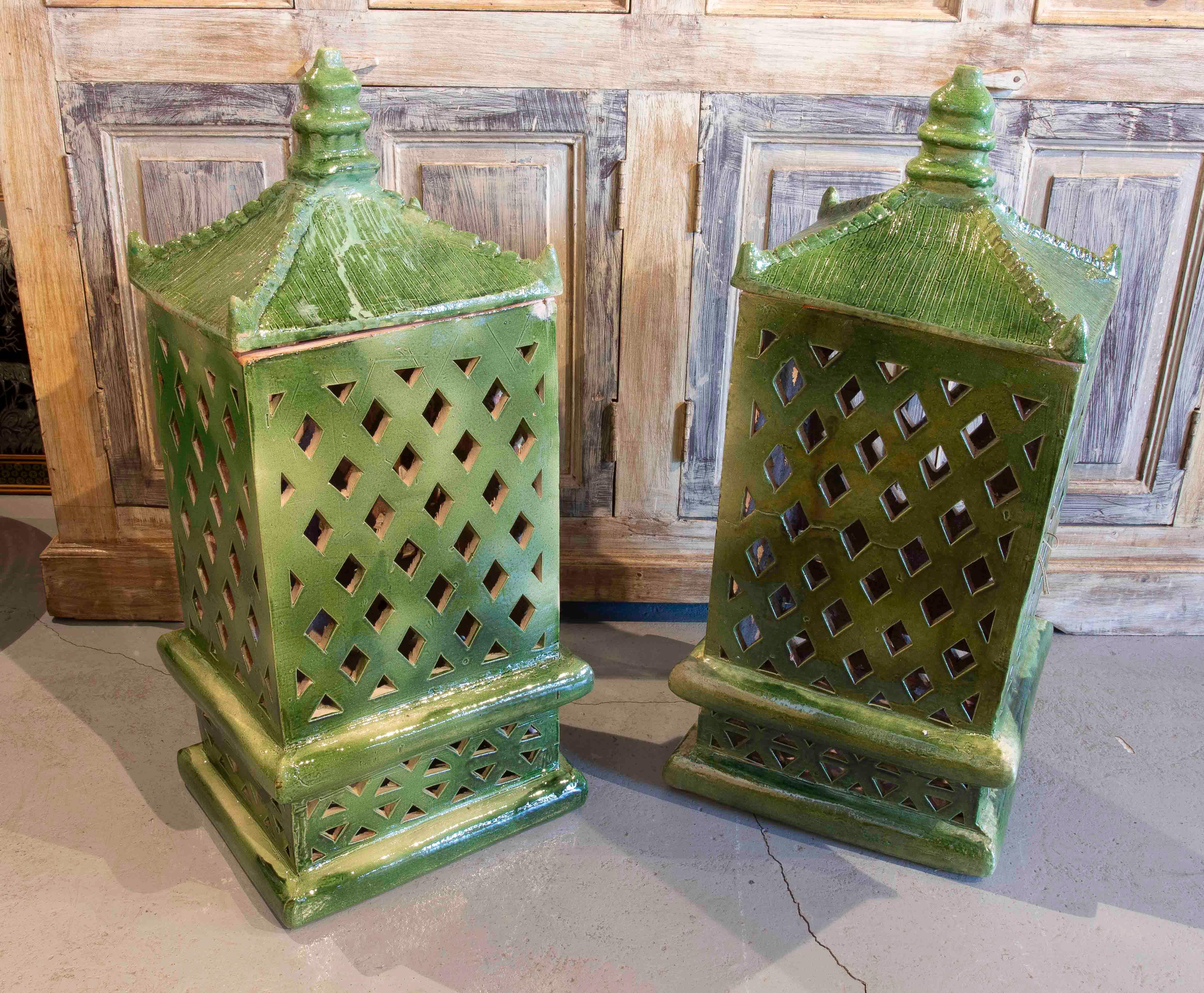 Magnífica pareja de faroles de cerámica vidriada en un intenso esmalte verde. Su diseño de celosía geométrica permite el paso de la luz, creando un decorativo juego de sombras. La estructura de base cuadrada se eleva hasta un tejado rematado con un