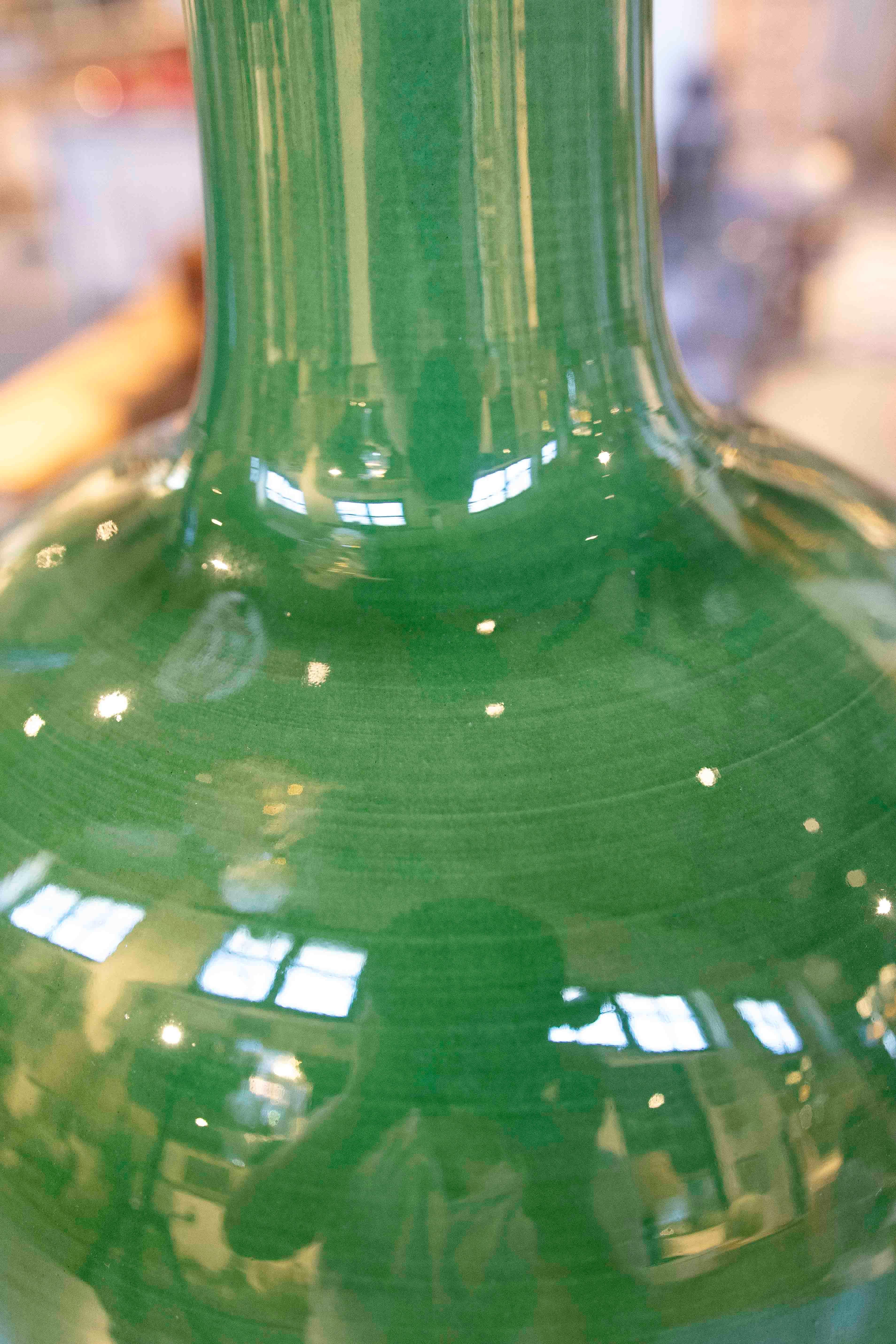 A striking pair of table lamps crafted from glazed ceramic in a deep green hue, with a glossy glaze finish that enhances their elegance and decorative character. The design combines a globular base with an elongated, slender neck, evoking