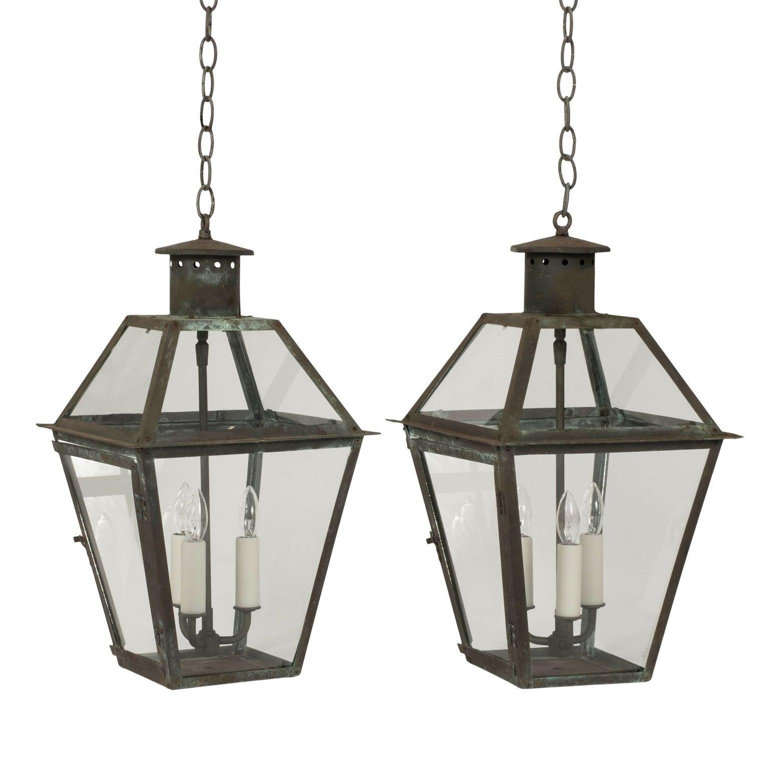 Pair of green verdigris copper lanterns circa 1910-1939. Rivet construction. Glass paneled. Newly wired with three drop clusters each. Candelabra size sockets. Each includes four feet of chain and a canopy. Handsome natural patina and subtle color