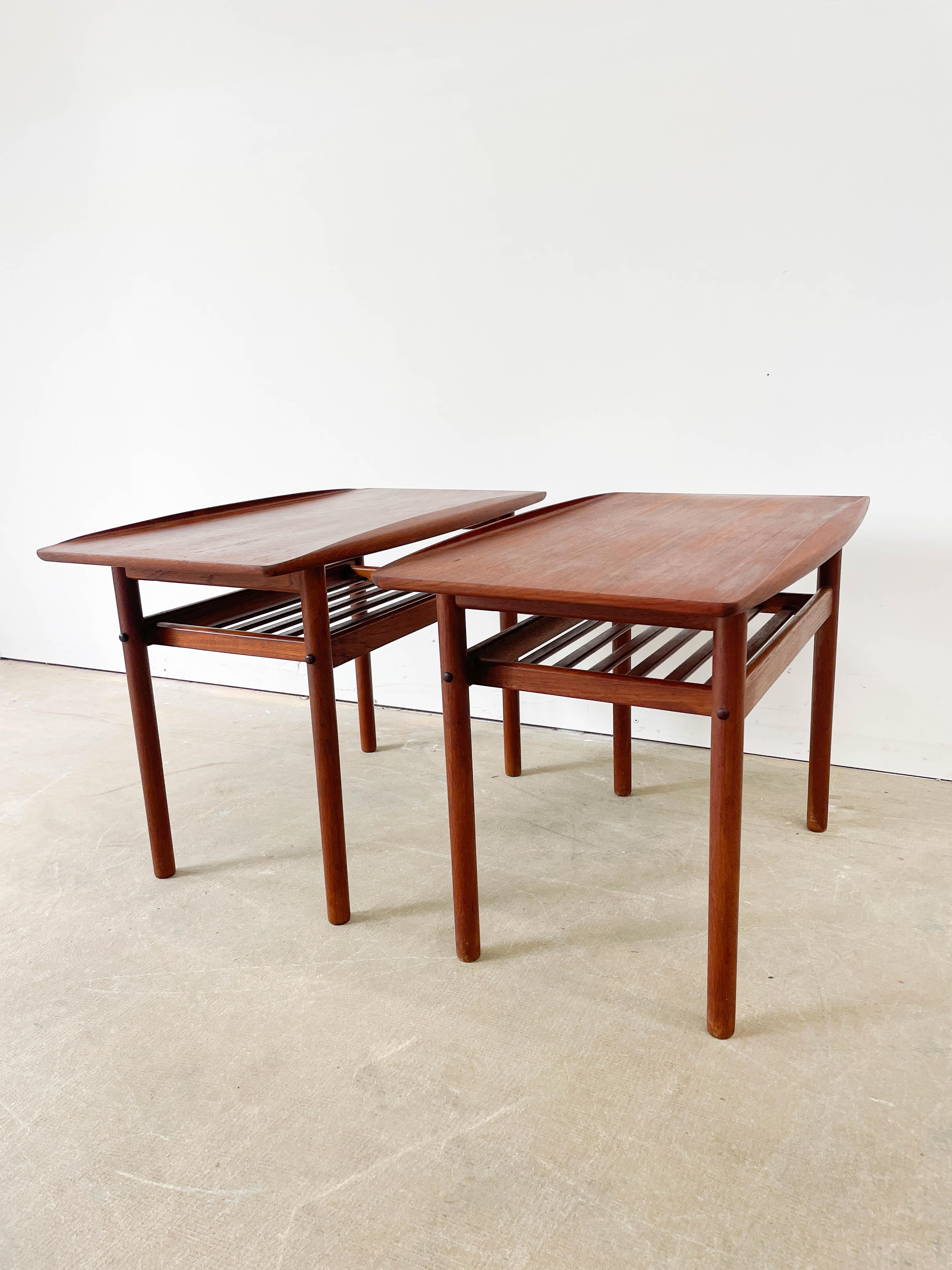 A pair of teak side tables designed by Grete Jalk and made by P. Jeppesen in Denmark in the 1950s. Beautiful teak tops with sculpted edges that resemble breaking waves and a useful slatted shelf beneath. Both tables have the Danish Furniture Maker's