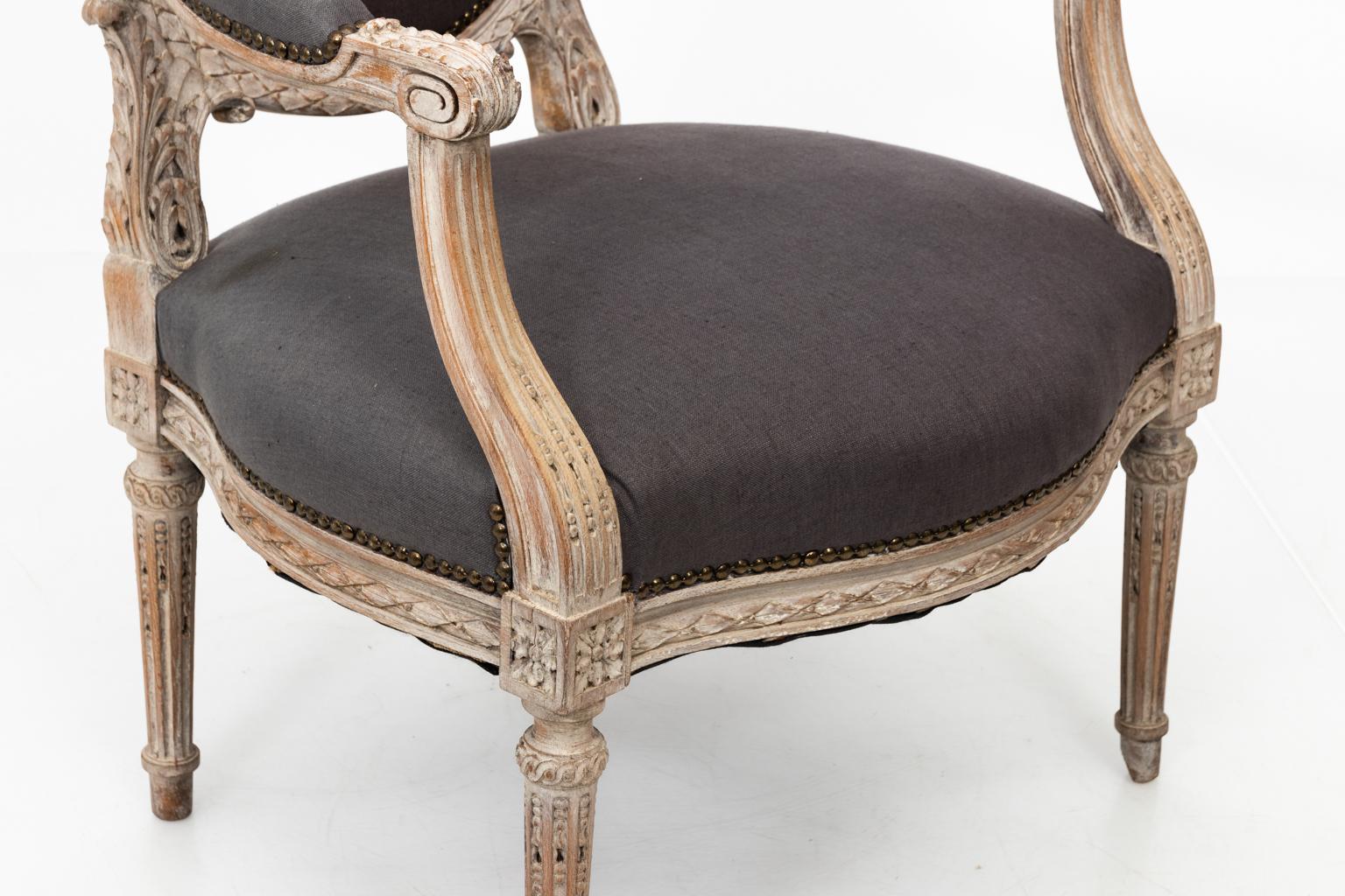 Pair of Louis XVI style walnut carved armchairs in grey upholstery from the South of France, circa 1820. The chairs feature a rounded back with brass nailhead trim. Please note of wear consistent with age including a worn finish to the paint.