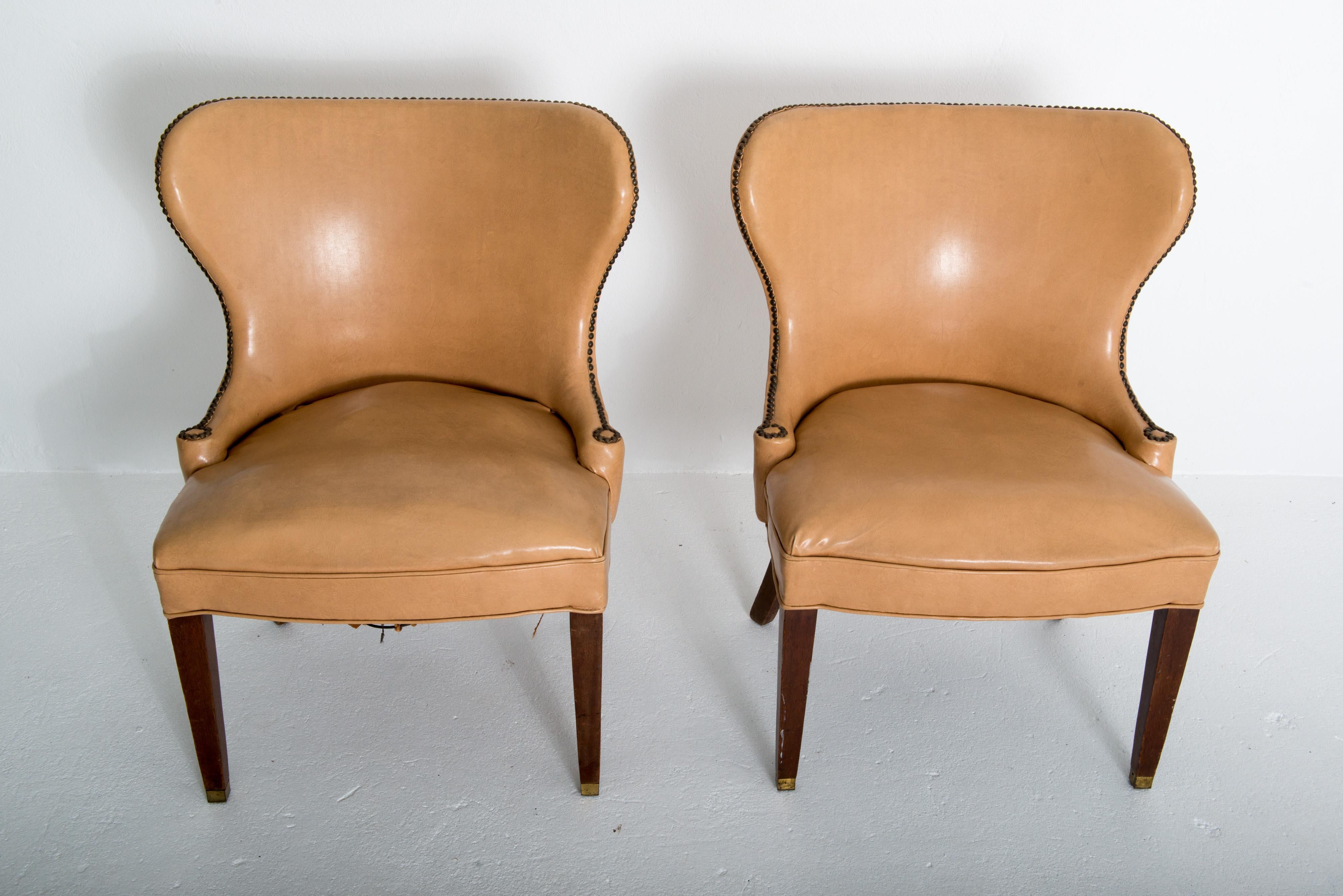 This is a pair of stunning Grosfeld House club chairs in the original beige-camel colored faux leather, nail head studded upholstery. They are roomy, comfortable, and substantial yet sculptural and stylish. Legs are smooth tapered stained hardwood.