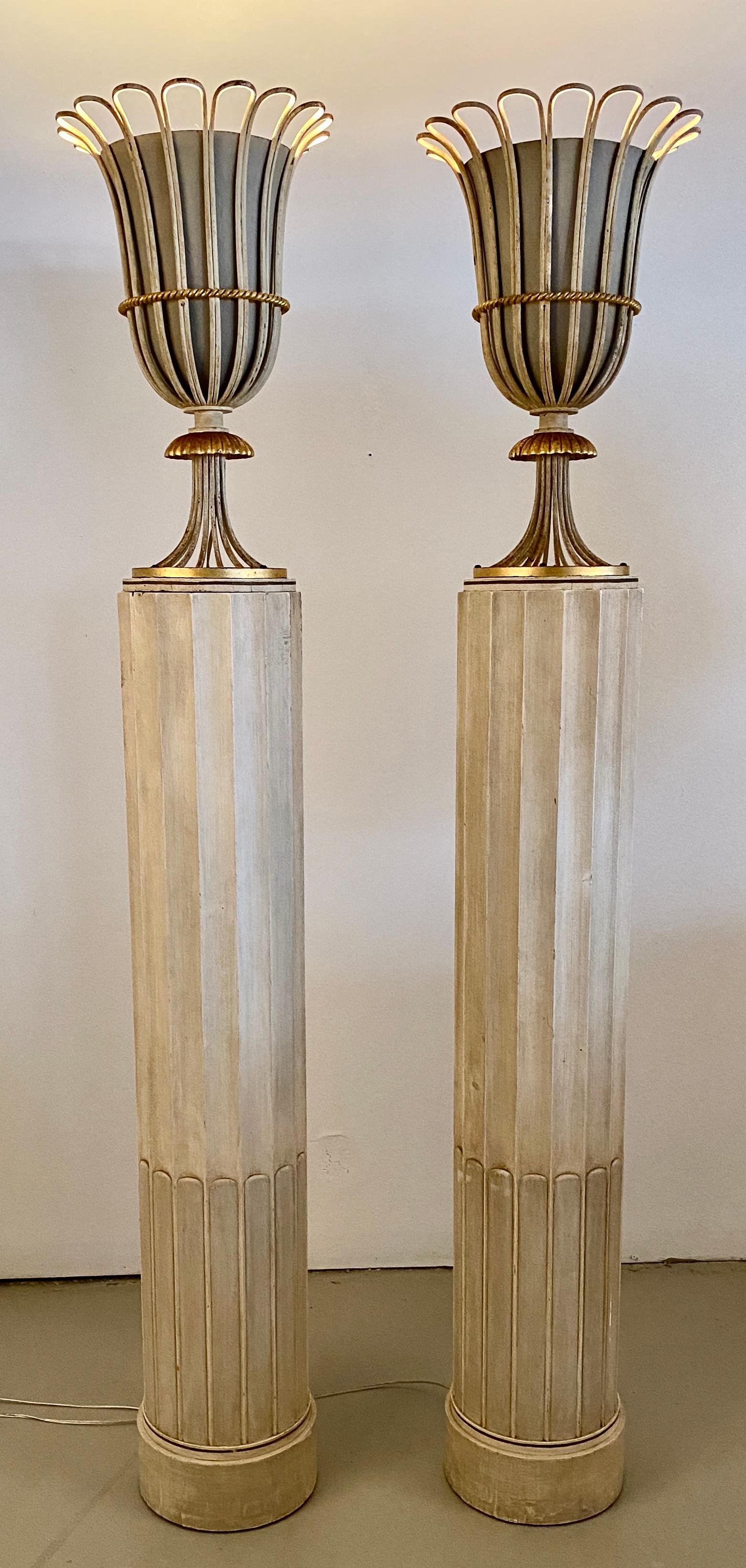 Totally glam pair of column-form torchieres made by Grosfeld House in true Hollywood Regency style. The fluted column bases are wood, the urn shaped lighting fixtures are metal with hand gilded details. The lights have been newly rewired but are