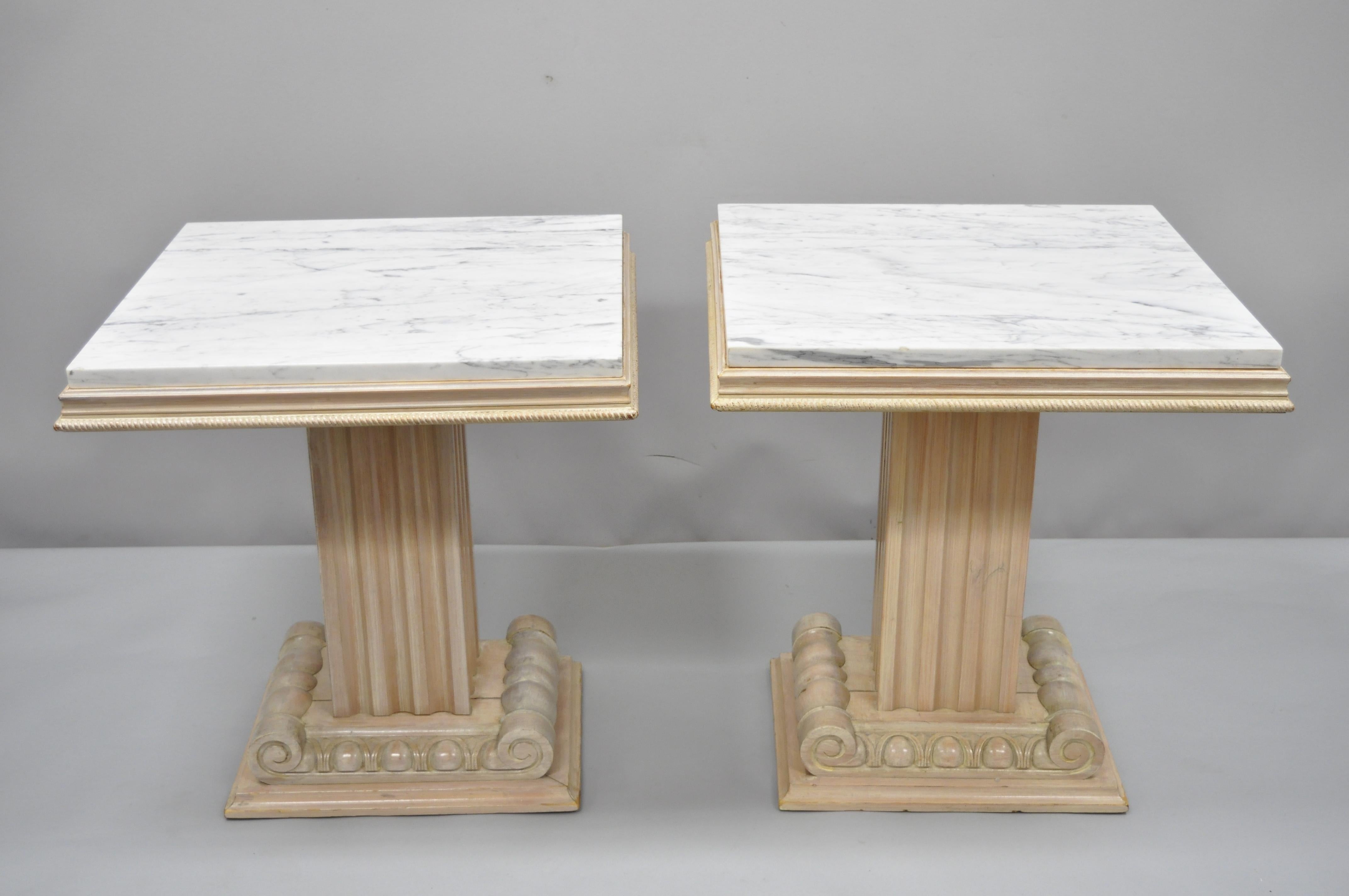 Pair of Grosfeld House Hollywood Regency ionic column pedestal base marble-top side tables. Item features solid carved wood bases, white marble tops, red leather tops underneath, cream washed distressed finish, nicely carved details, original label,