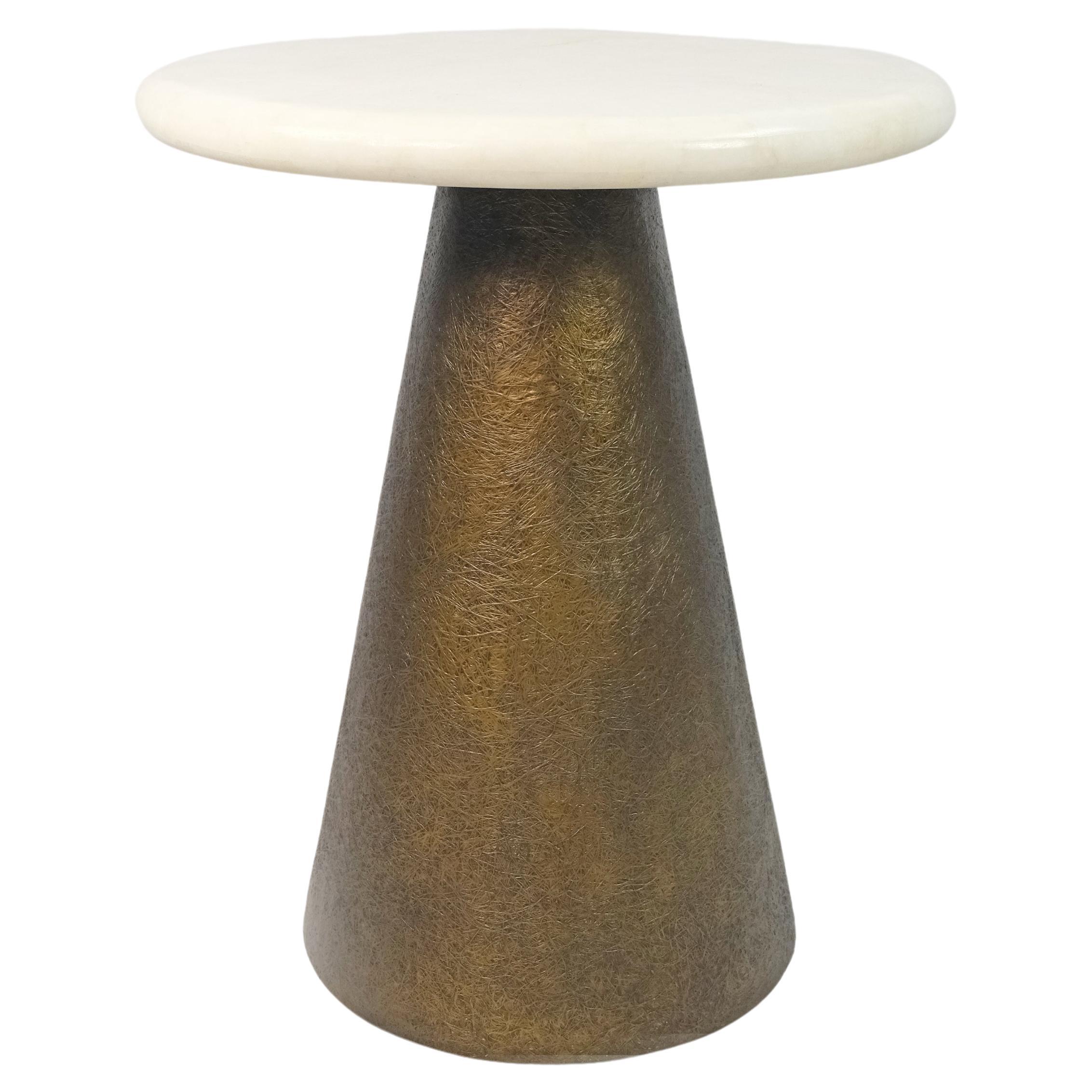 This side table is made of a round white rock crystal marquetry top.
The conical base is made of wood with a bronzed semi-raw glass fiber inlaying.
The semi raw finishing brings an interesting texture thanks to the nice rounded shape of the