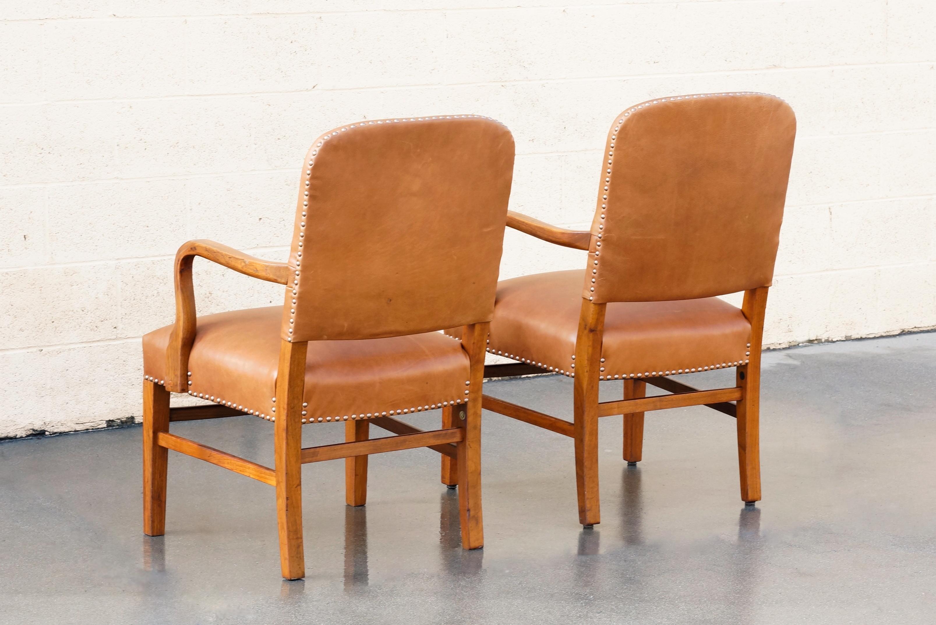 Stately pair of Gunlocke armchairs from 1948. Refinished oak and reupholstered in camel-colored leather with hammered upholstery tacks. Oak arms feature subtle carved detailing along the curves. Please note: foot risers have been replaced, not