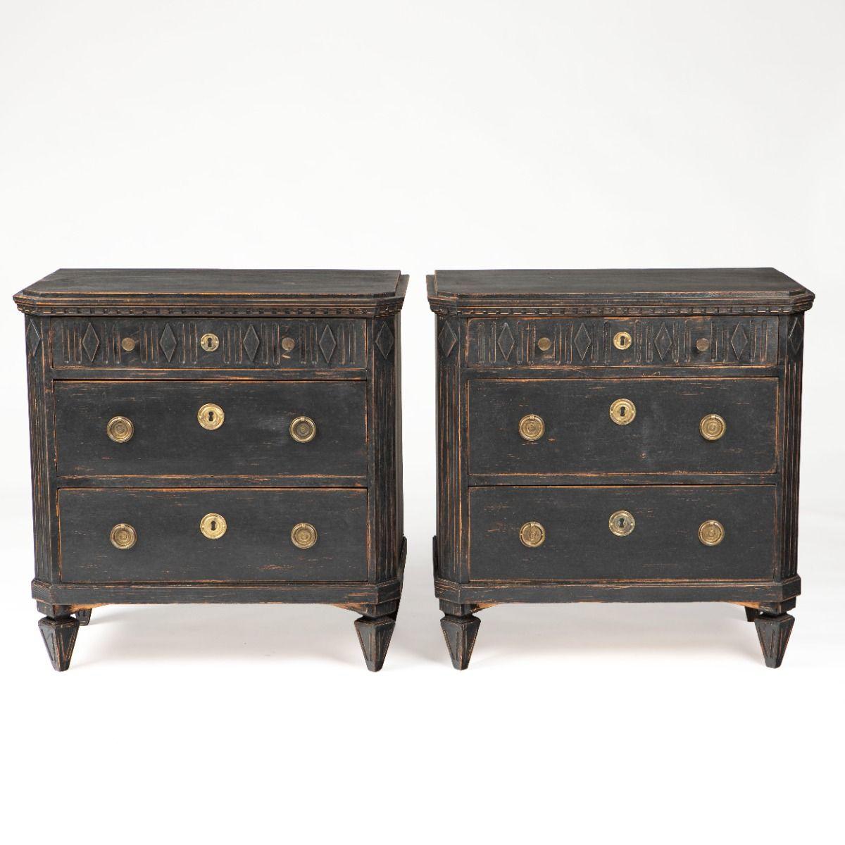 A pair of Swedish commodes in Gustavian style, dating from circa 1840–1860.

Executed in black painted pine and mounted with patinated brass fittings, the commodes feature a profiled top with dentil frieze, a front with three drawers - the upper