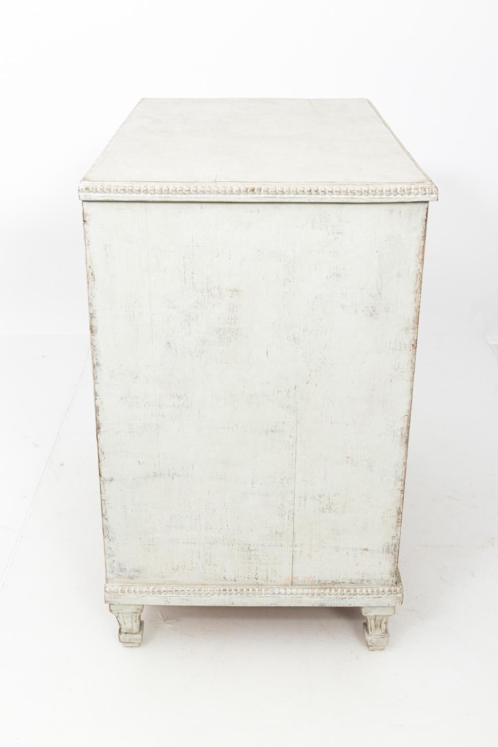 Pair of painted Swedish Gustavian style chests with three drawers and dentil trim, circa 19th century. The piece also features metal pulls. Please note of wear consistent with age.