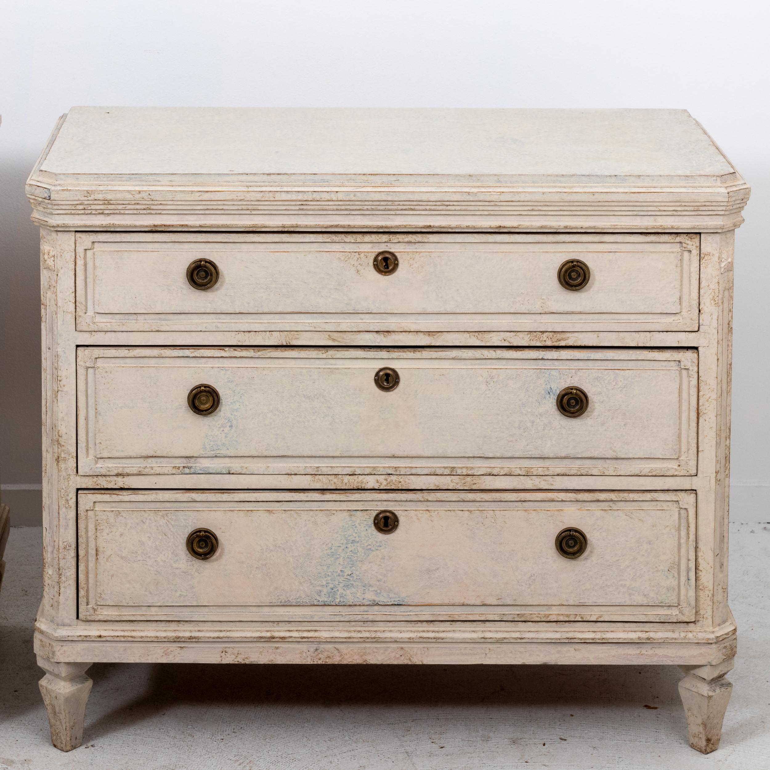 Circa 20th century pair of Gustavian style chest of drawers in a Swedish antique white color. The canted corners with carved rosette medallions are typical of the Gustavian style. Please note of wear consistent with age including chips and minor